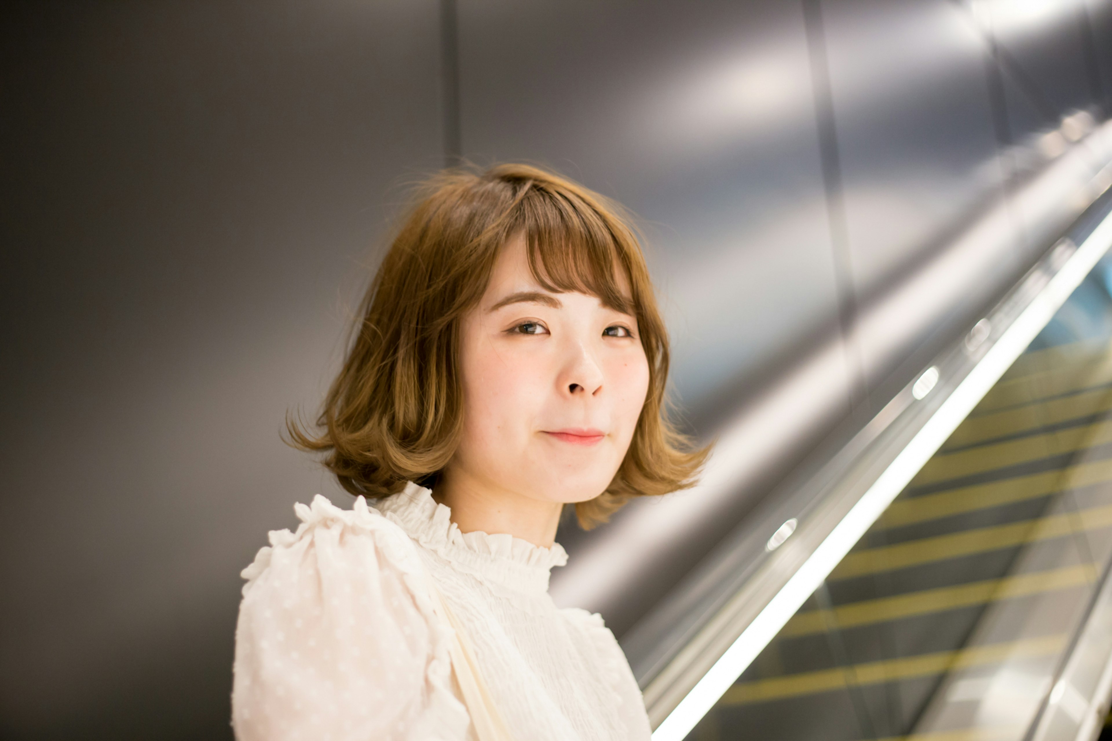 Young woman smiling in a white blouse with a modern escalator in the background