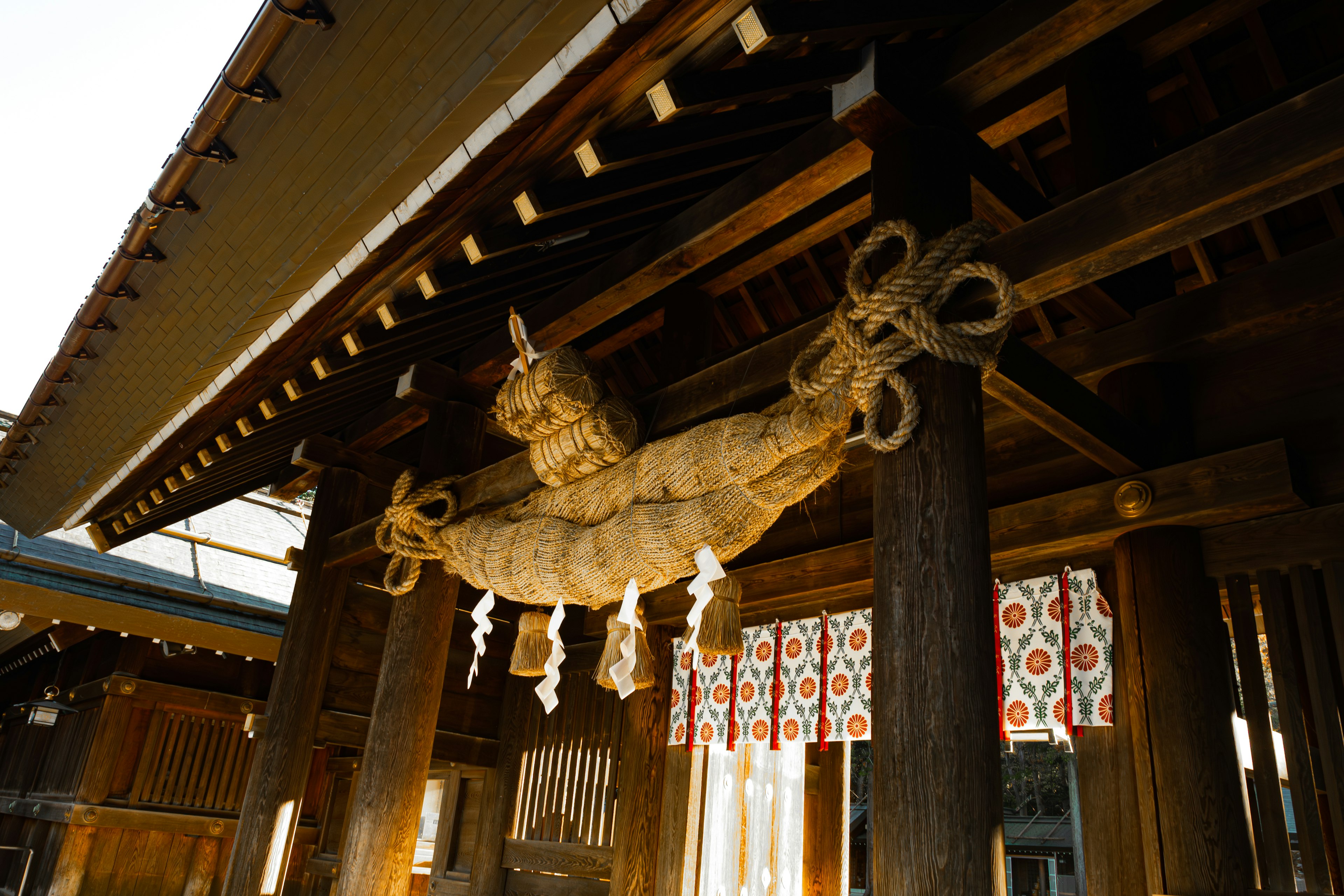 Large rope decoration hanging at the entrance of a traditional shrine with red patterned curtains