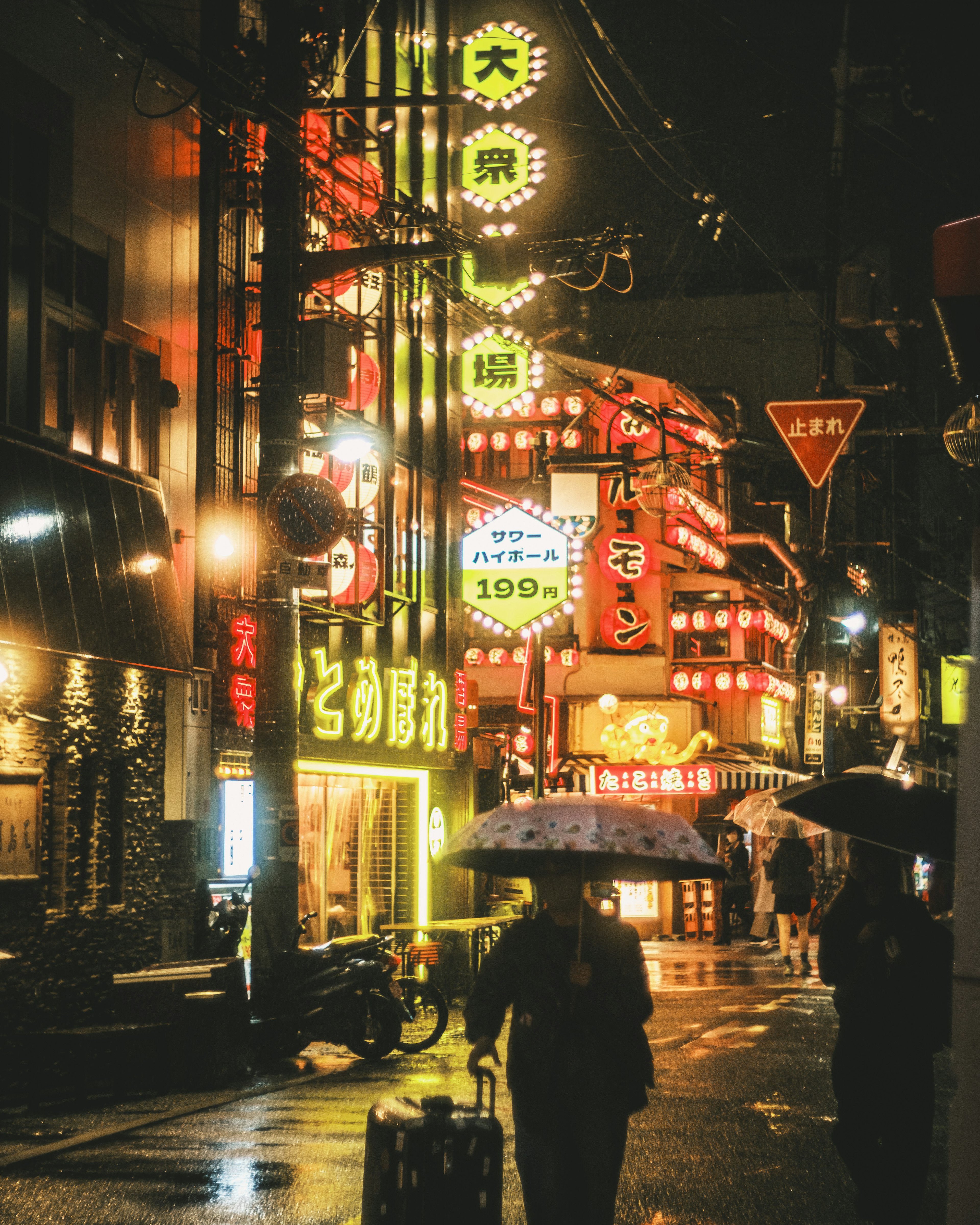 A person holding an umbrella walking in a street illuminated by bright neon signs in the rain