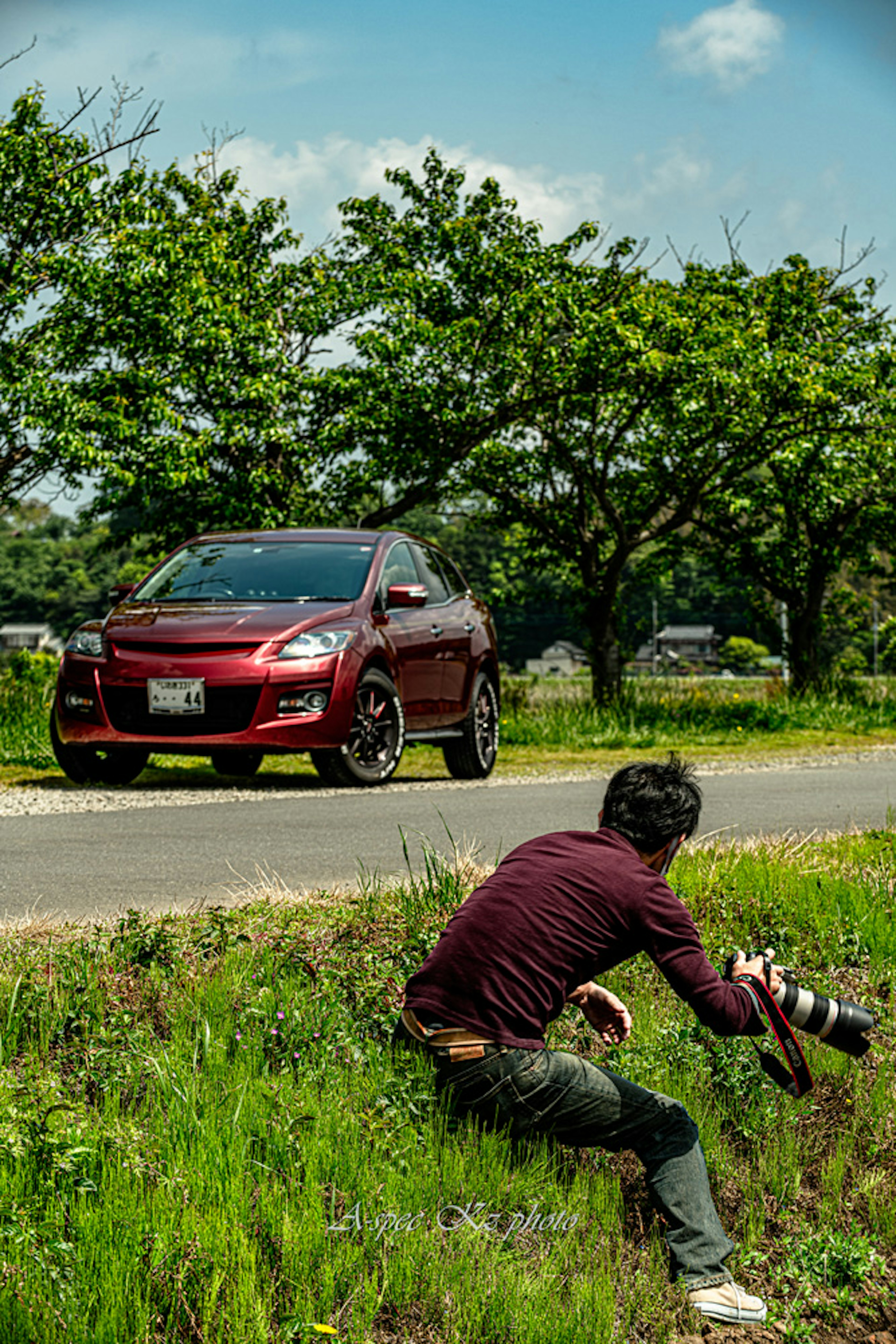 赤い車とカメラマンが緑の草原で撮影している風景