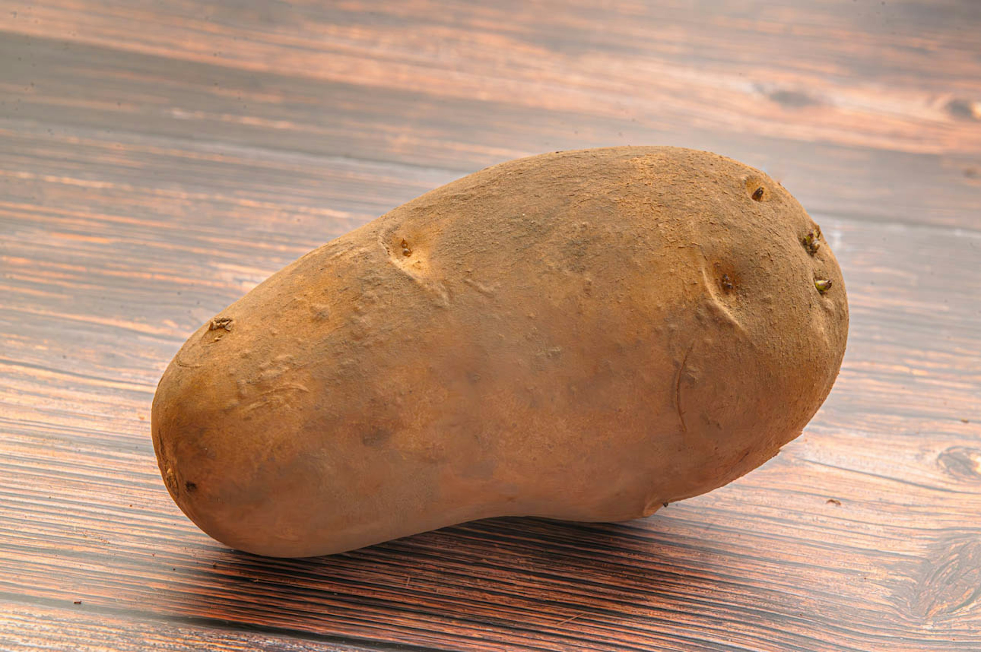 A potato resting on a wooden table surface