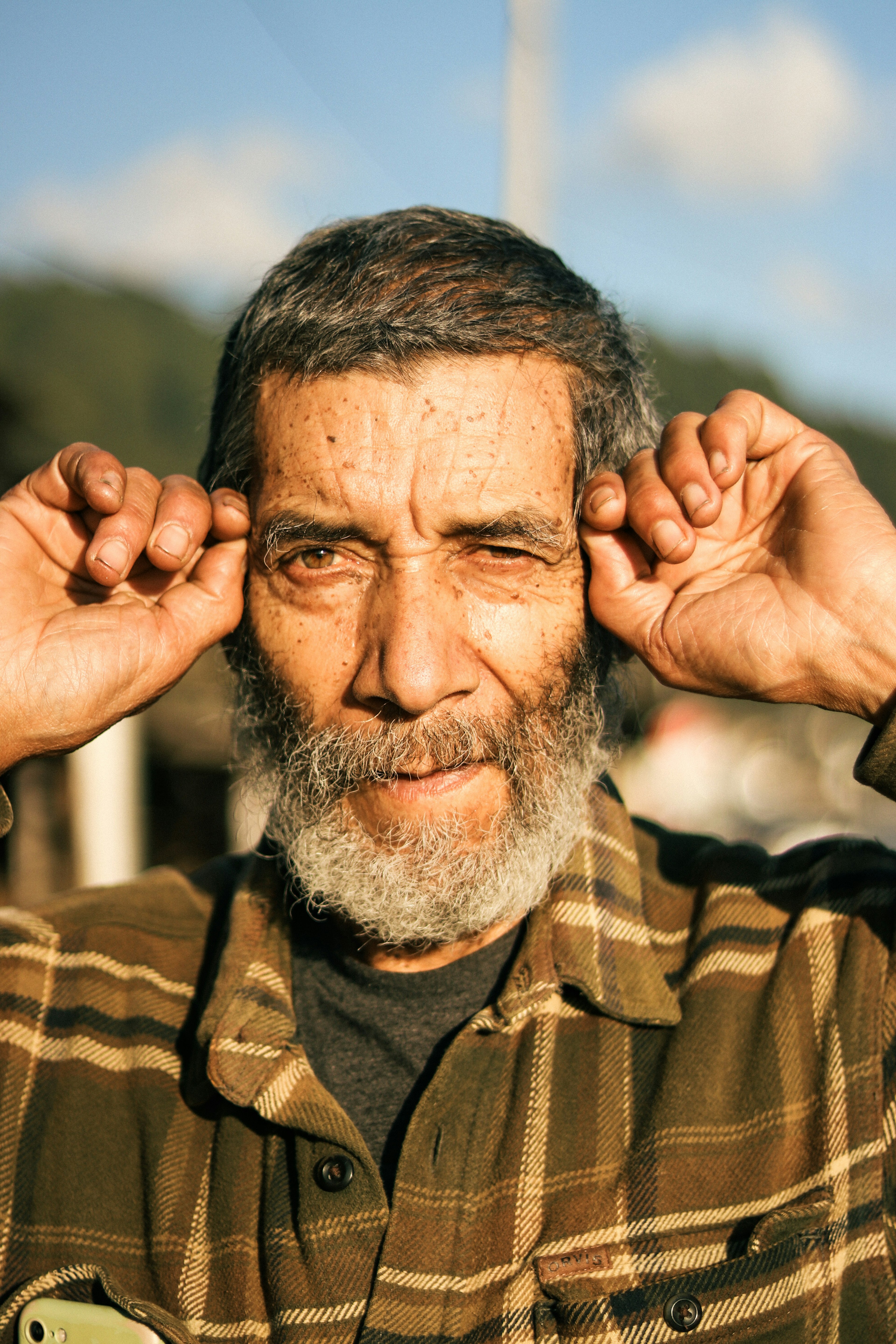 Portrait of a man holding his ears wearing a checkered shirt bright background