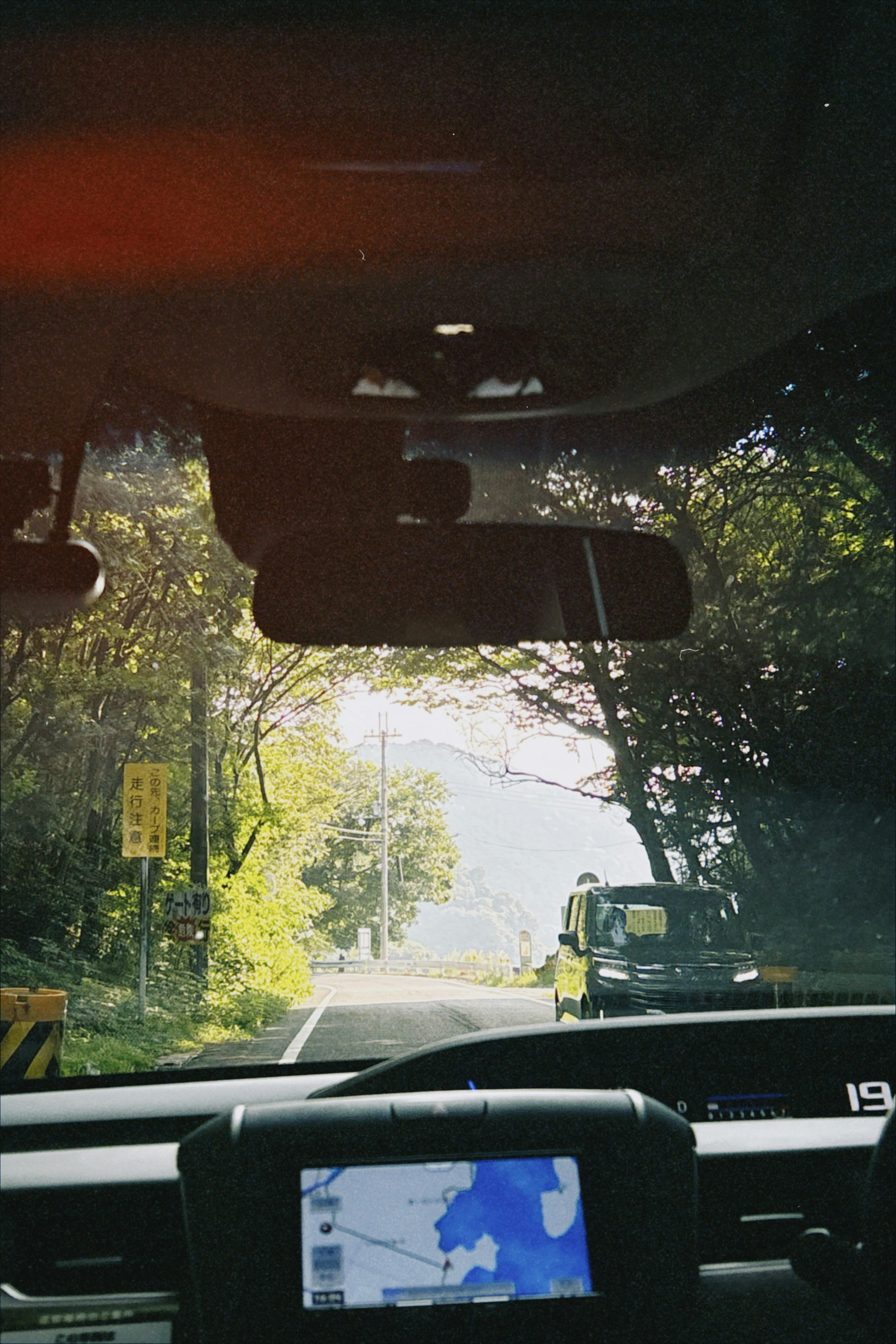 View from inside a car showing trees and road navigation system sunlight filtering through foliage