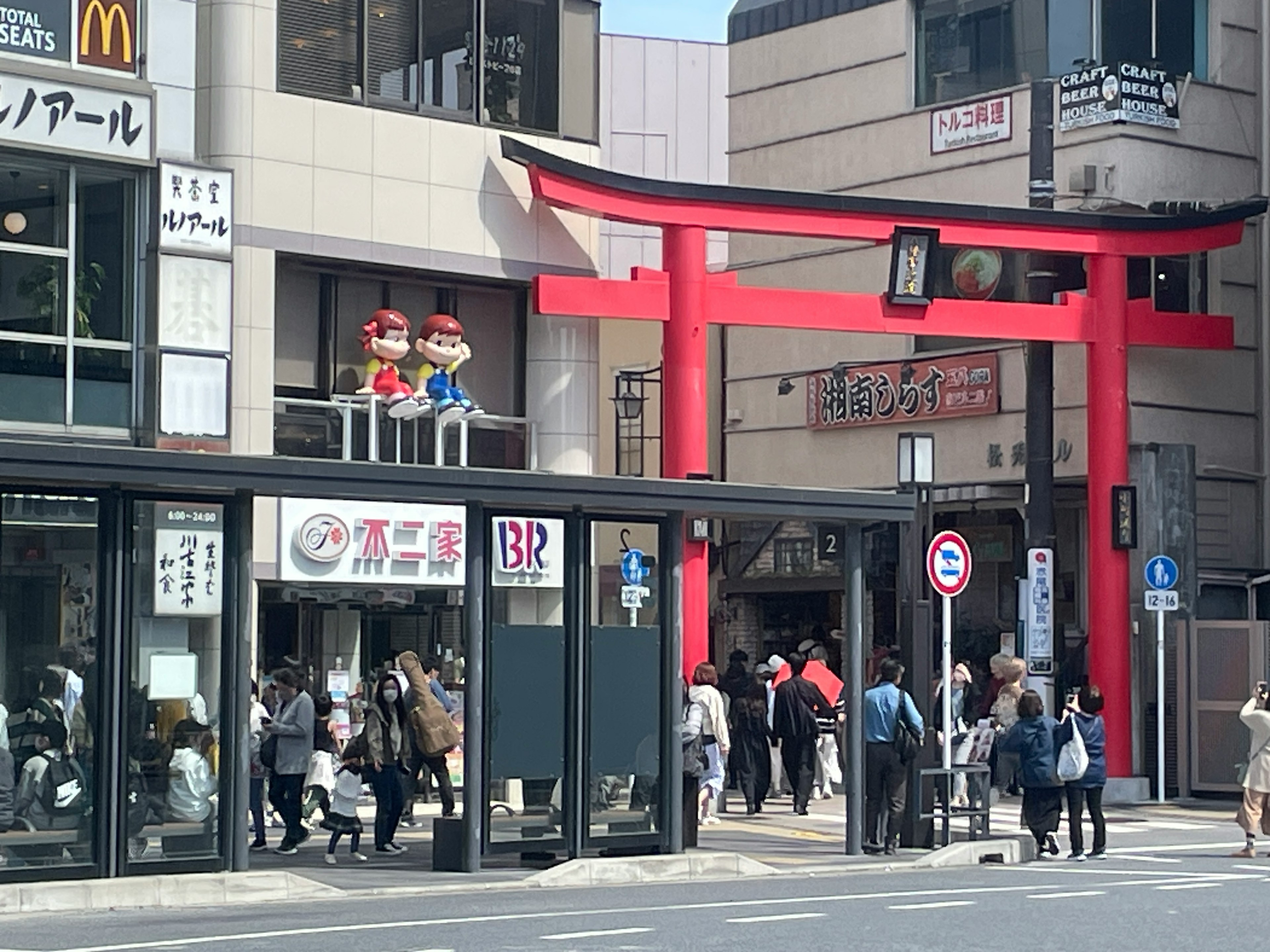 Eine lebhafte Straßenszene mit einem roten Torii-Tor und zahlreichen Menschen in einem belebten Geschäftsbereich