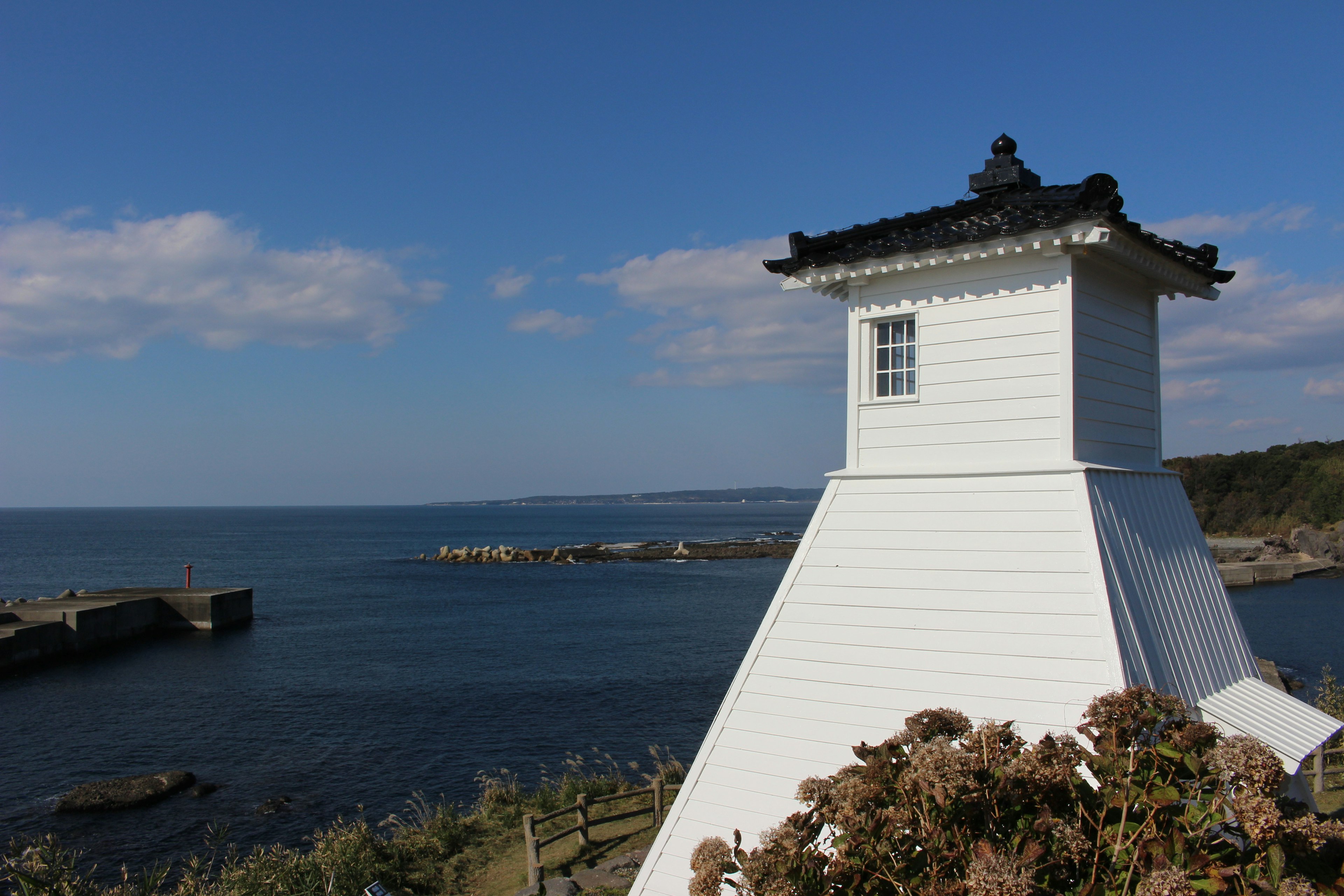 Ein weißer Leuchtturm steht vor dem Ozean und dem Himmel