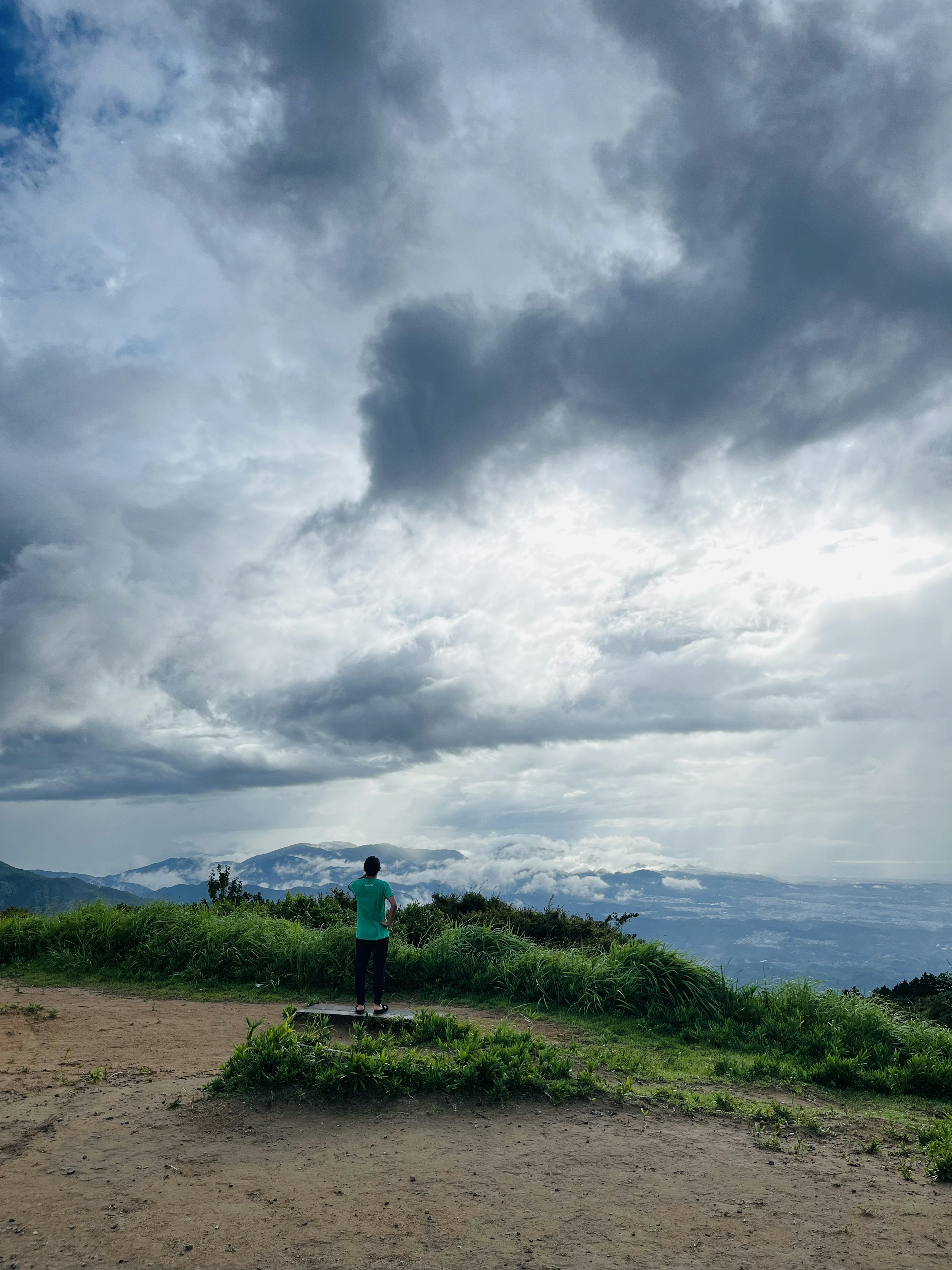 Persona de pie en una colina verde con cielo nublado