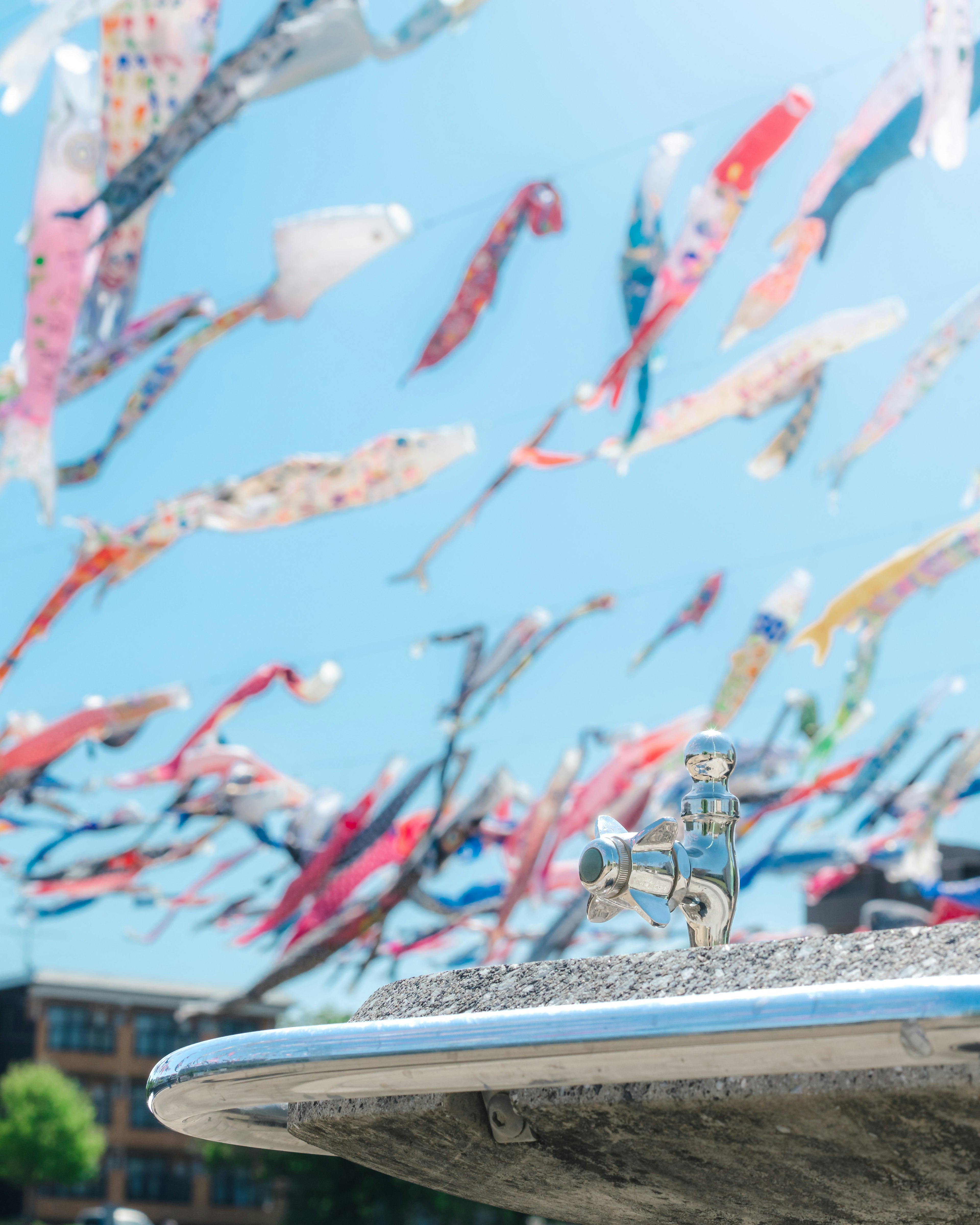 Des banderoles de carpes flottant sous un ciel bleu avec un robinet d'eau au premier plan