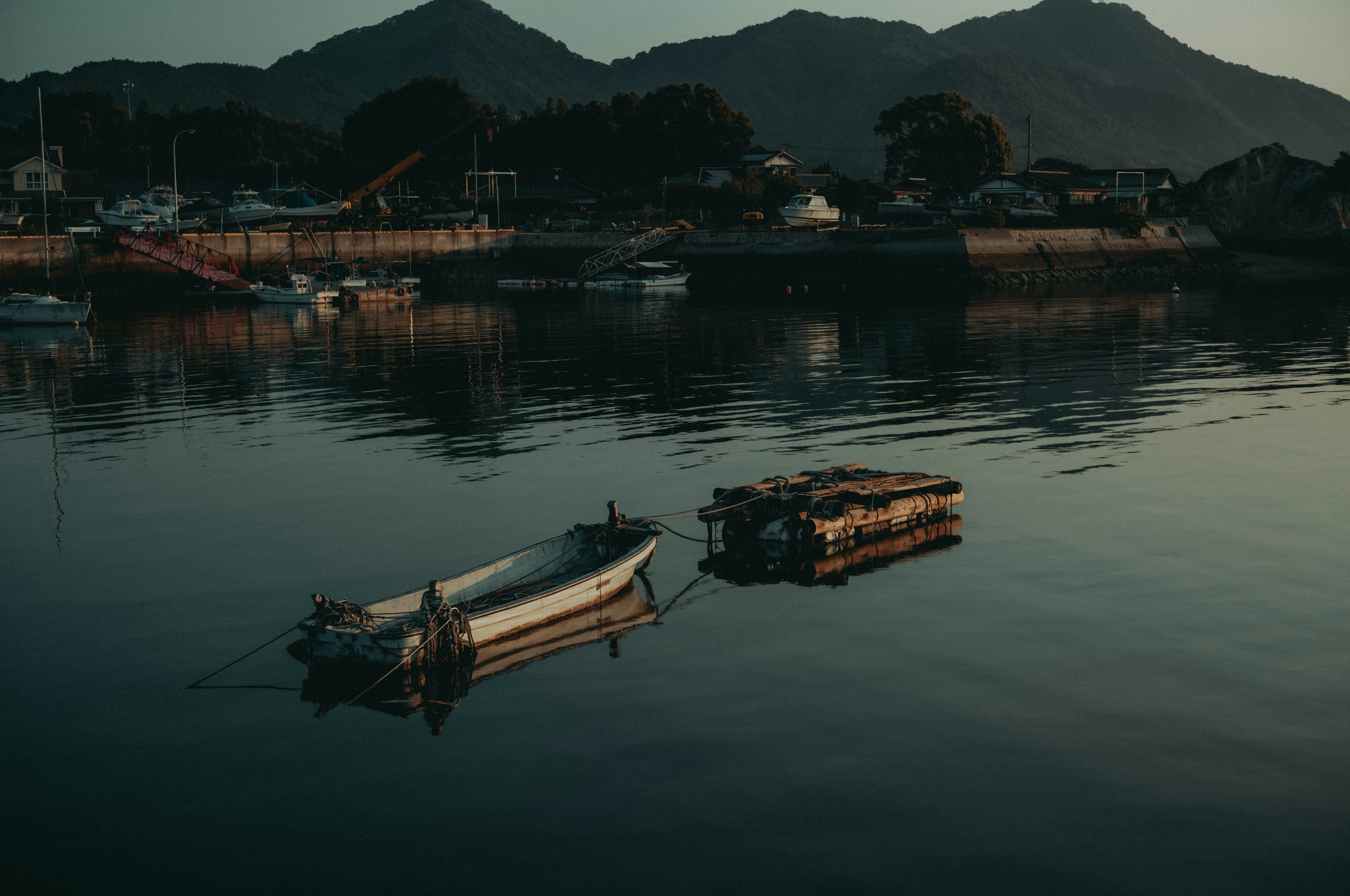 小船和筏子漂浮在平静的水面上，周围是山脉和宁静的港口