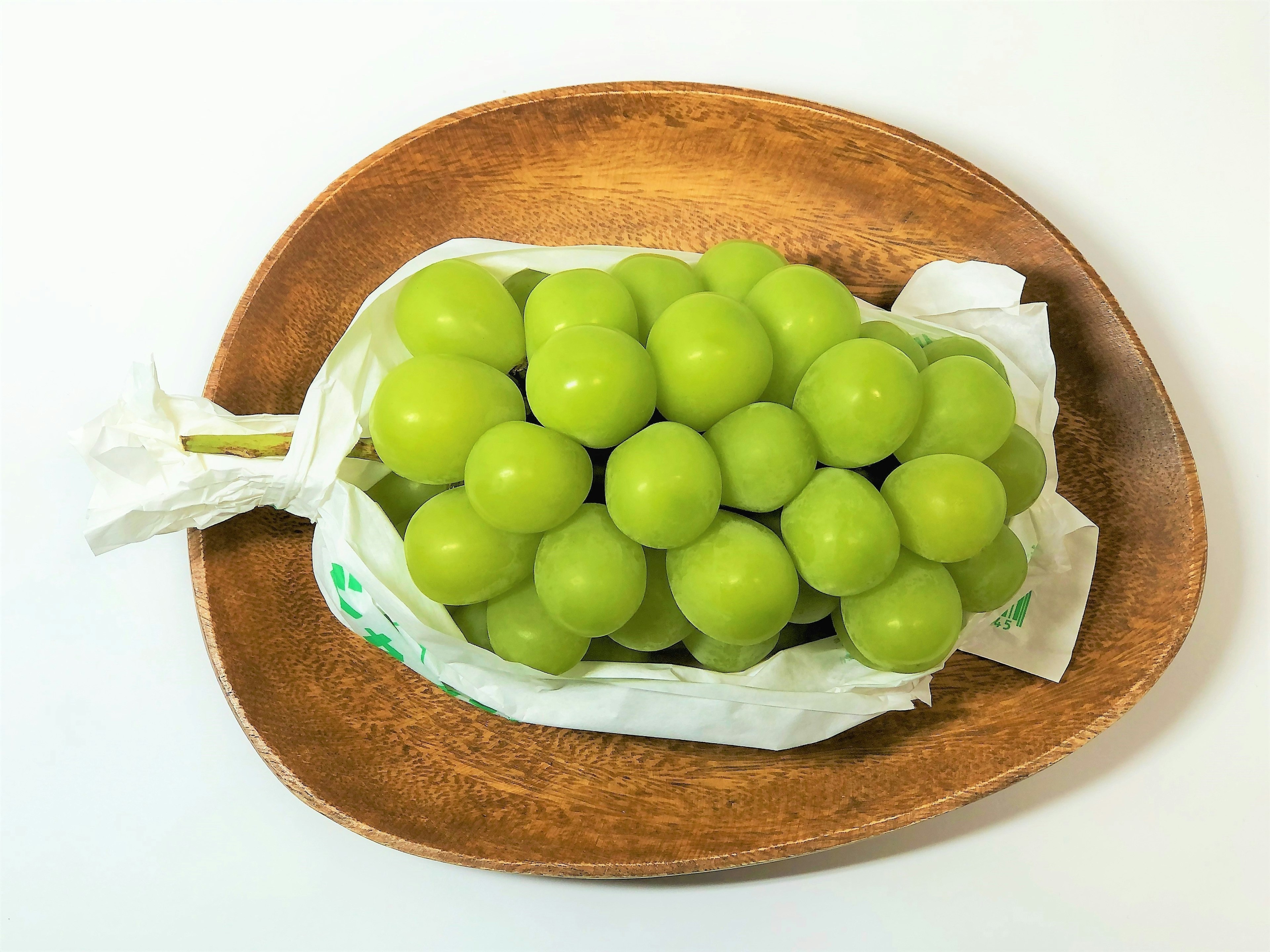 Uvas verdes en una bolsa blanca sobre un plato de madera