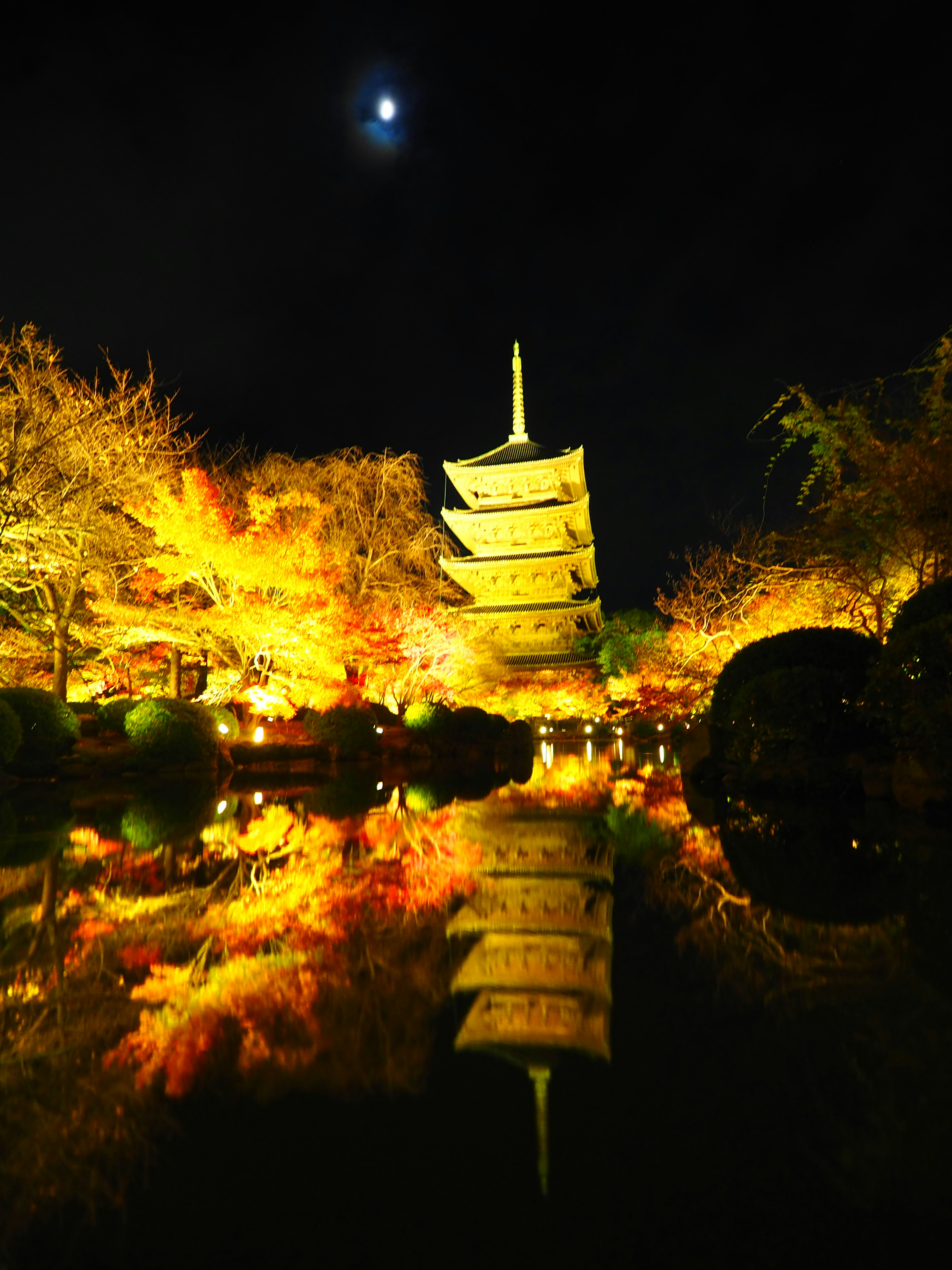 Vista nocturna de una pagoda rodeada de hojas de otoño coloridas y su reflejo