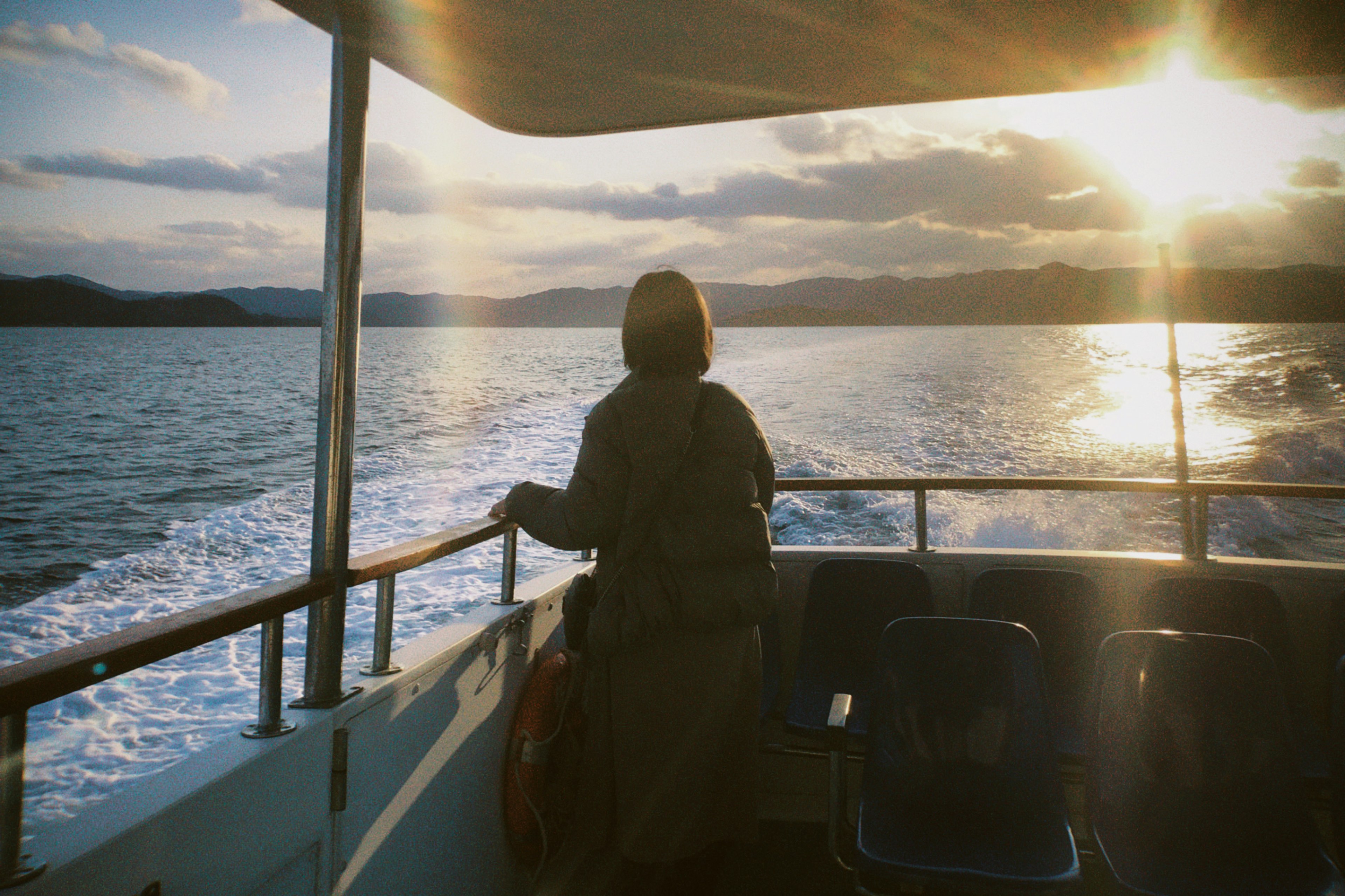 Person steht auf einem Boot mit Sonnenuntergang im Hintergrund ruhige Ozeansicht