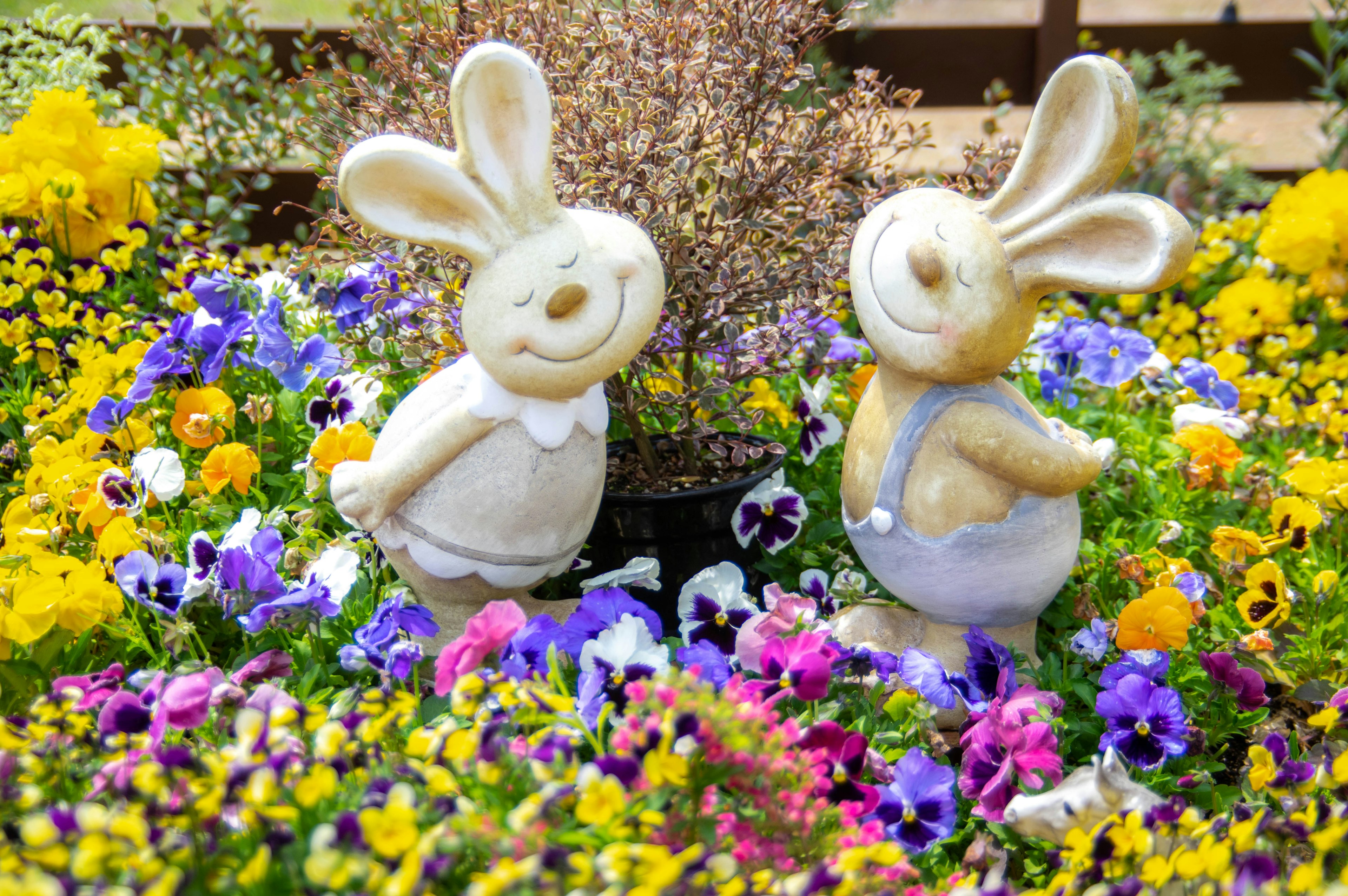 Two rabbit figurines surrounded by colorful flowers in a garden setting