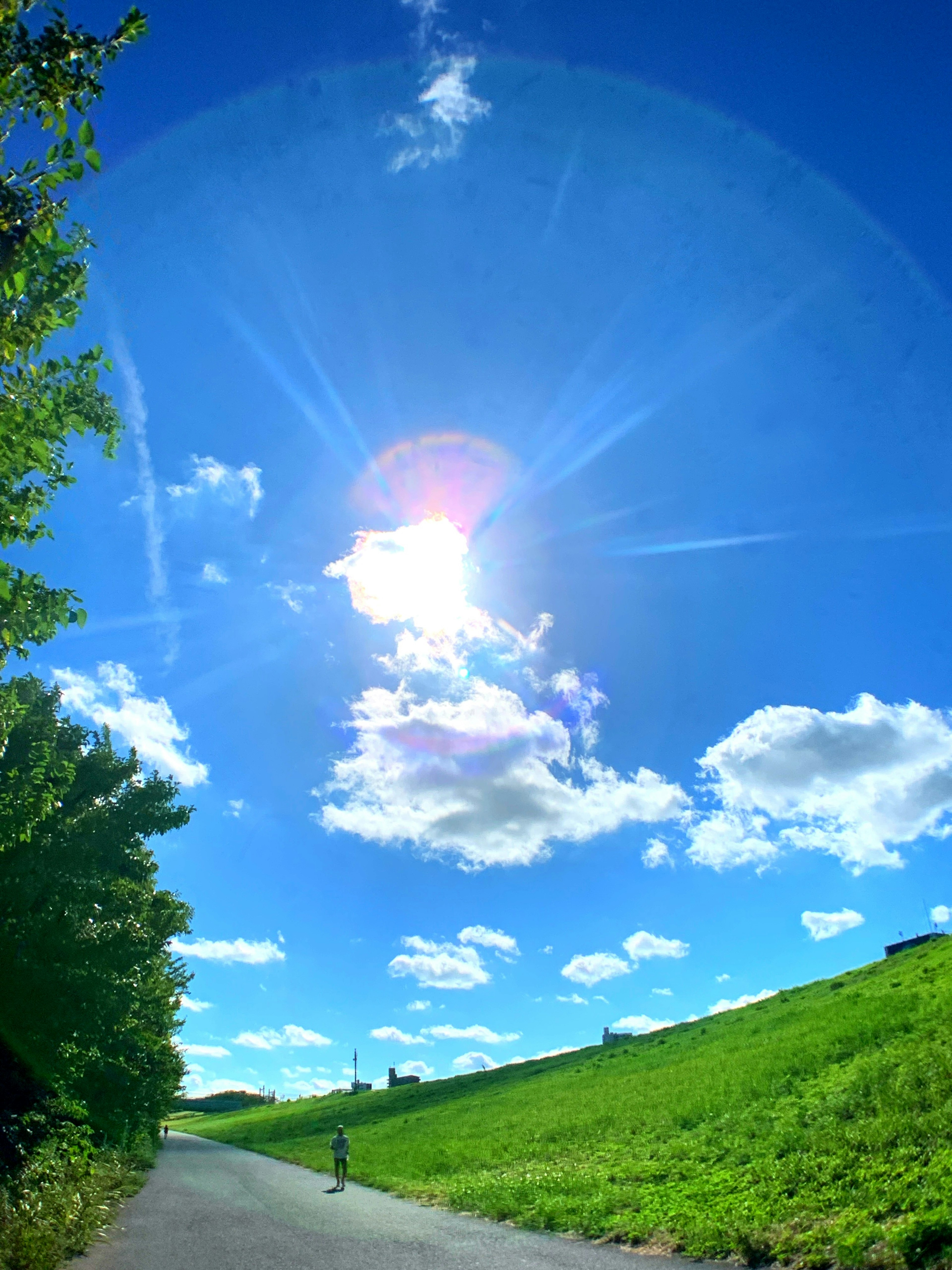 Bright blue sky with fluffy white clouds and shining sun over a green hillside