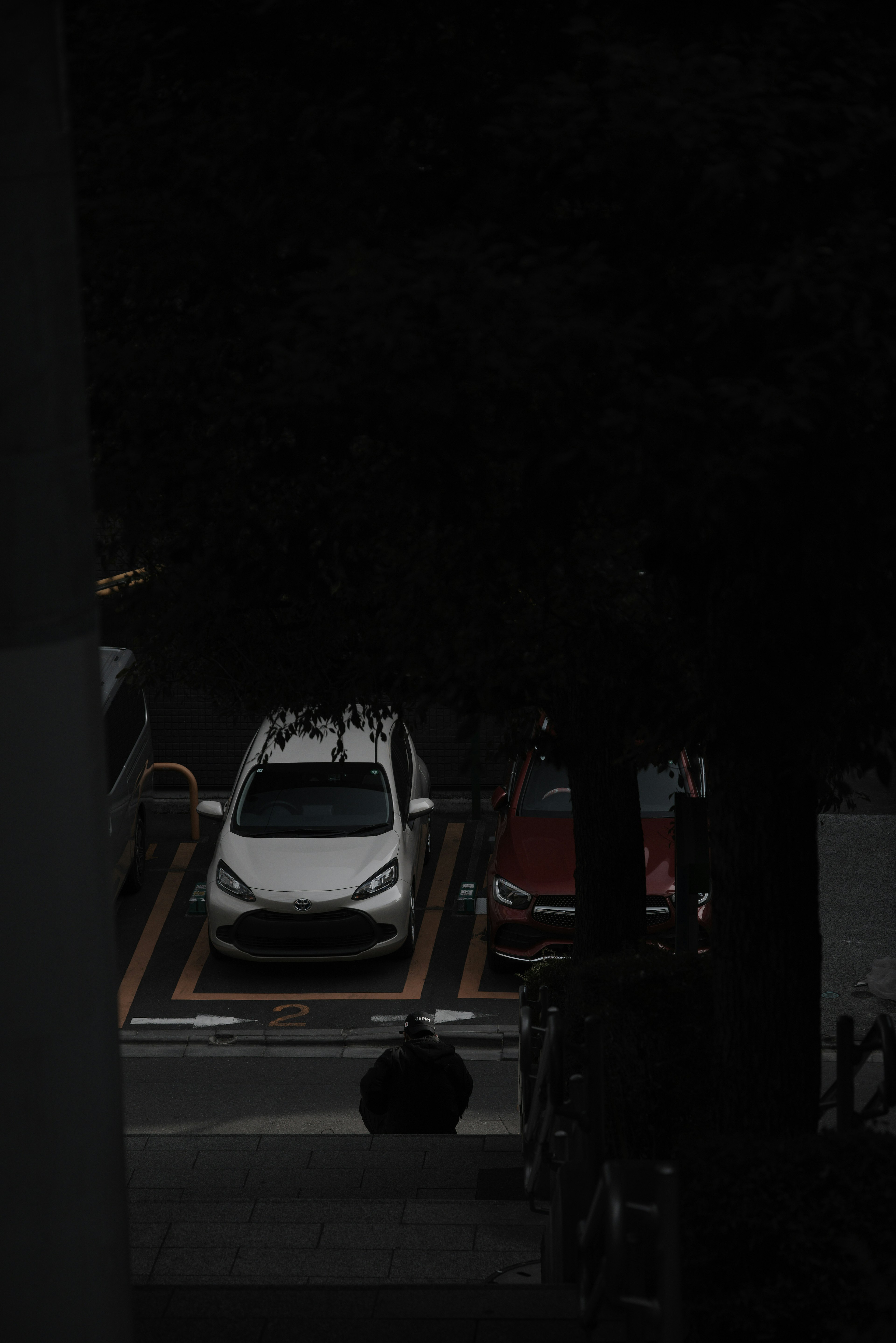 Un coche blanco y un coche rojo estacionados en un aparcamiento poco iluminado