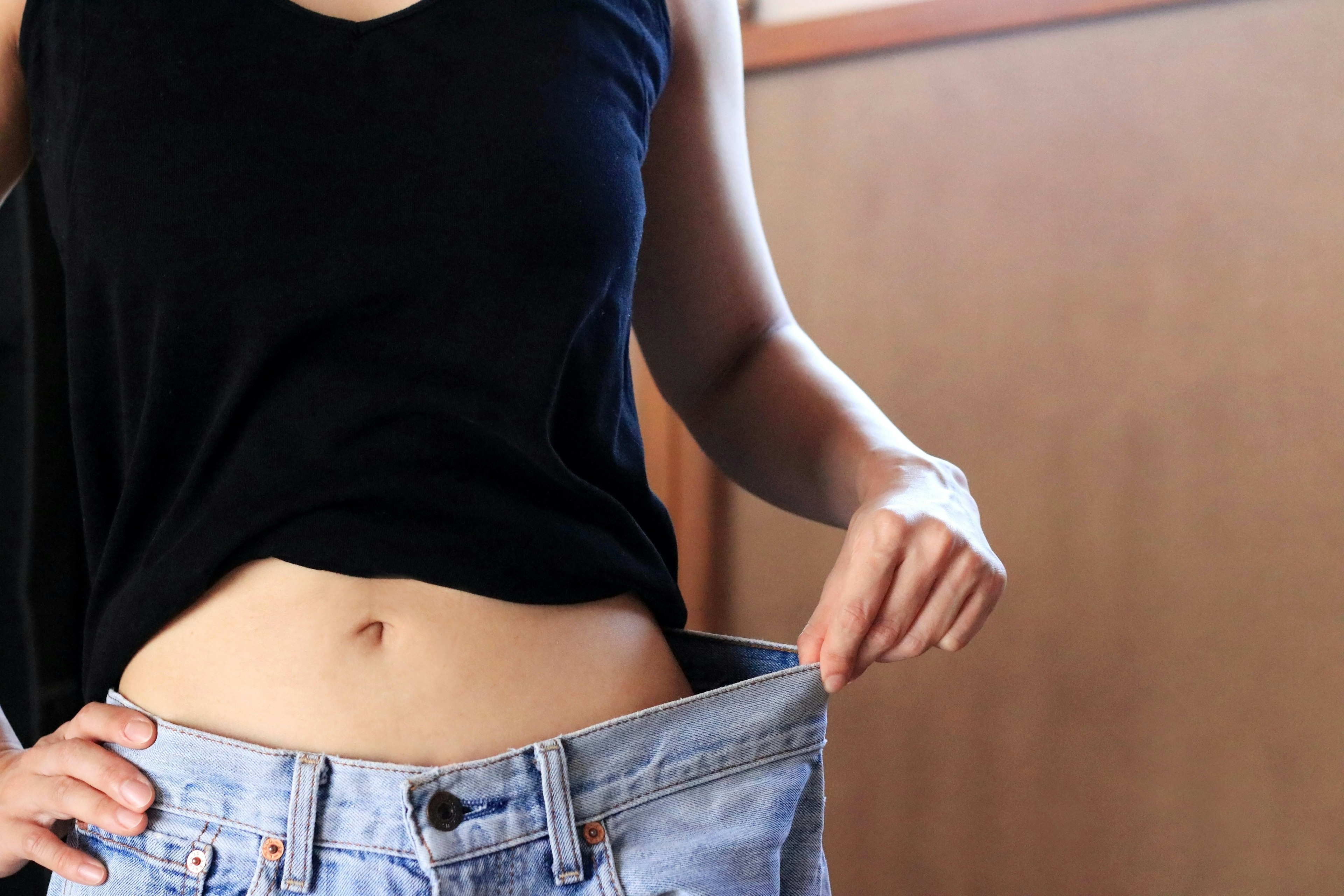 Mujer sosteniendo jeans grandes, usando una camiseta negra, cintura delgada