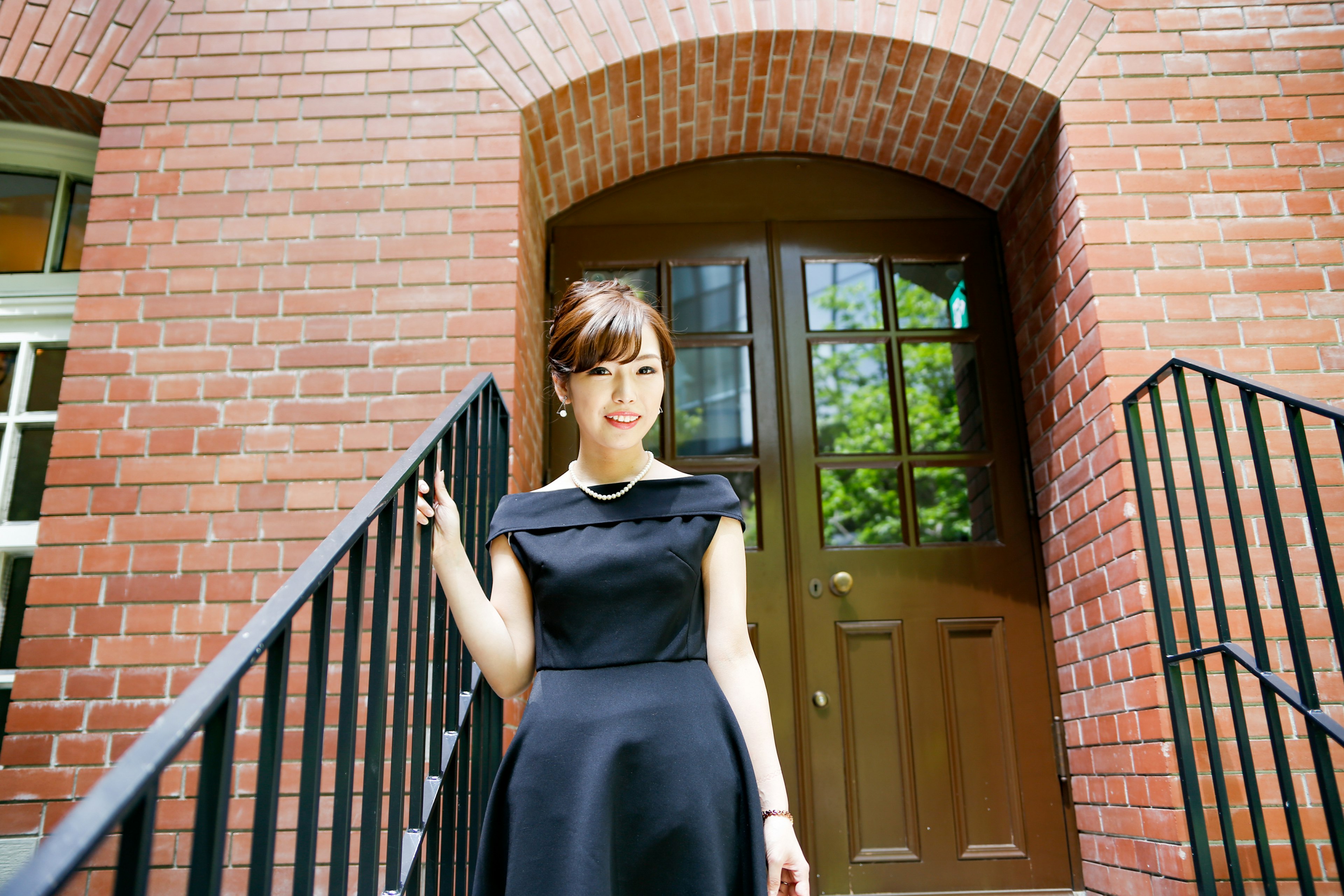 A woman in a black dress standing in front of a brick building