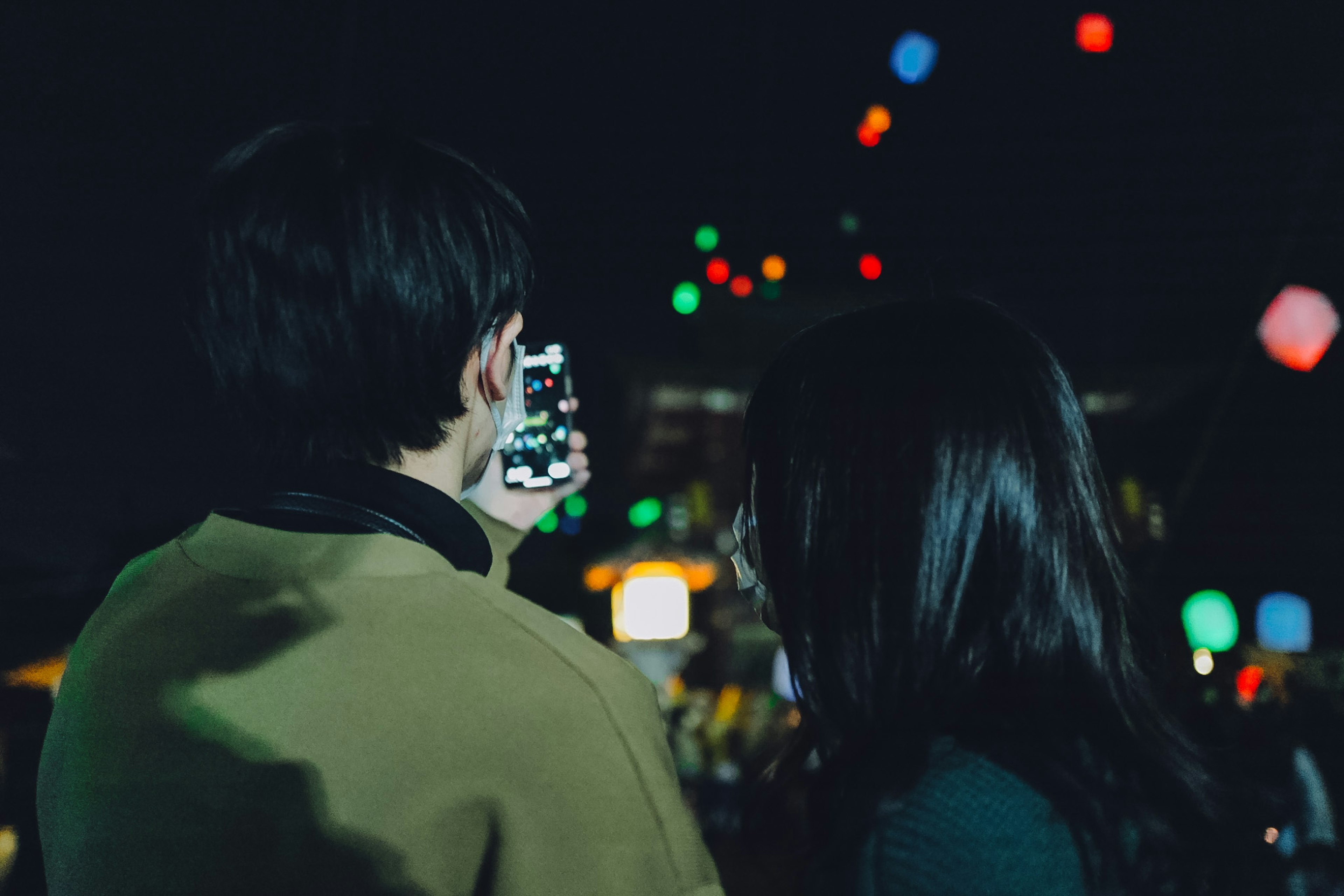 Pareja disfrutando de un festival nocturno con luces coloridas y un smartphone