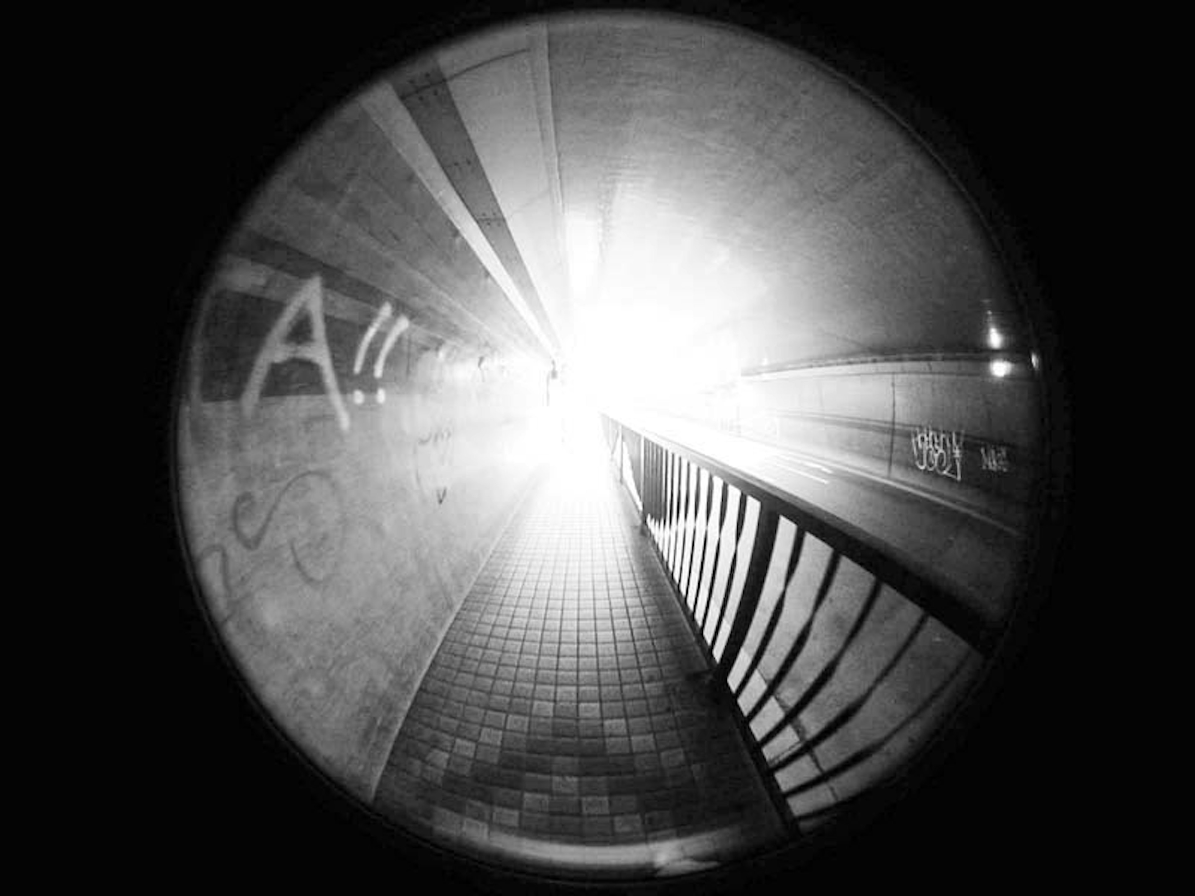 Interior de un túnel con luz brillante que entra líneas distintivas y barandilla de hierro