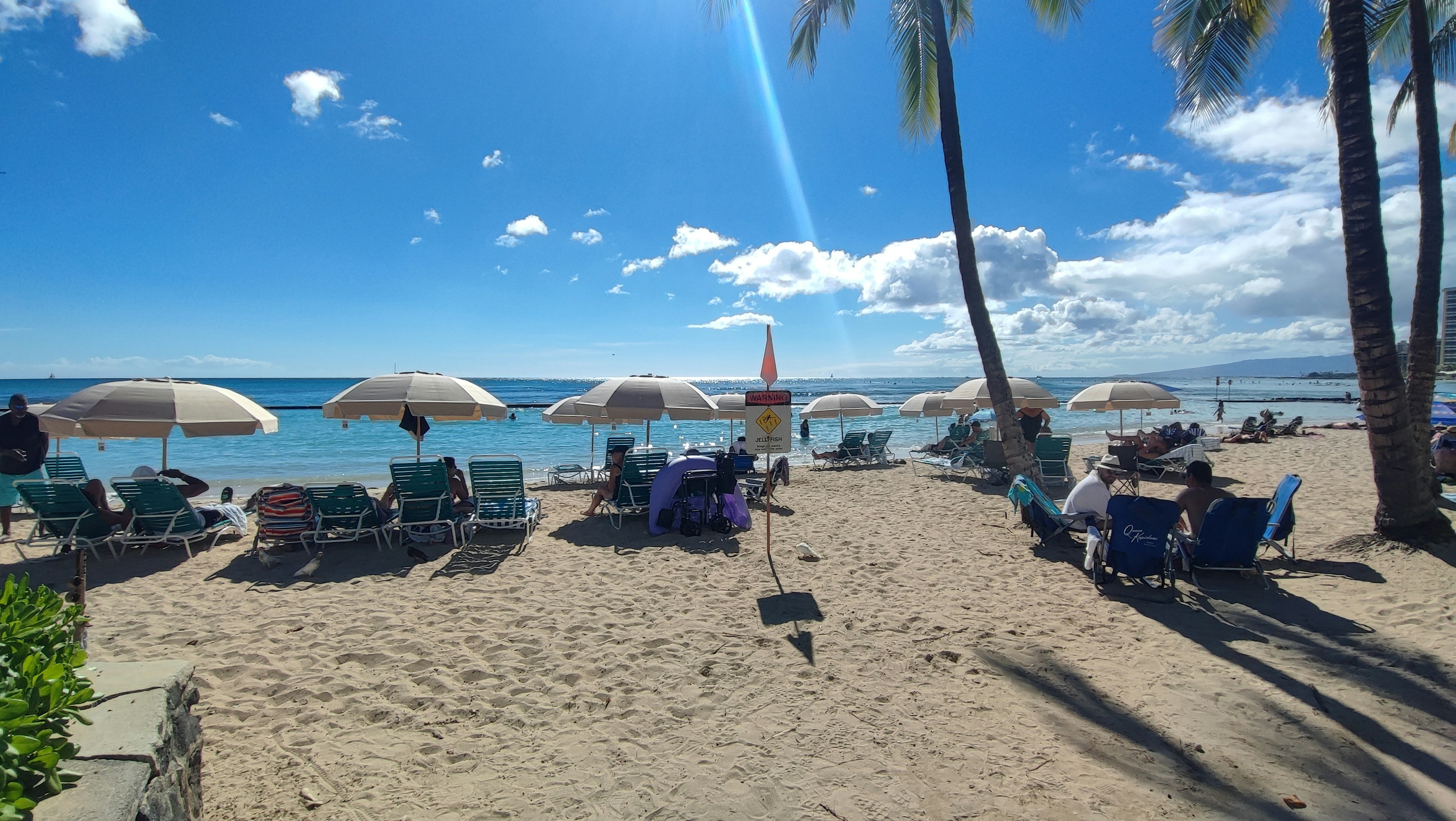 Strandszene mit Sonnenschirmen und Liegen am Sandstrand unter einem klaren blauen Himmel