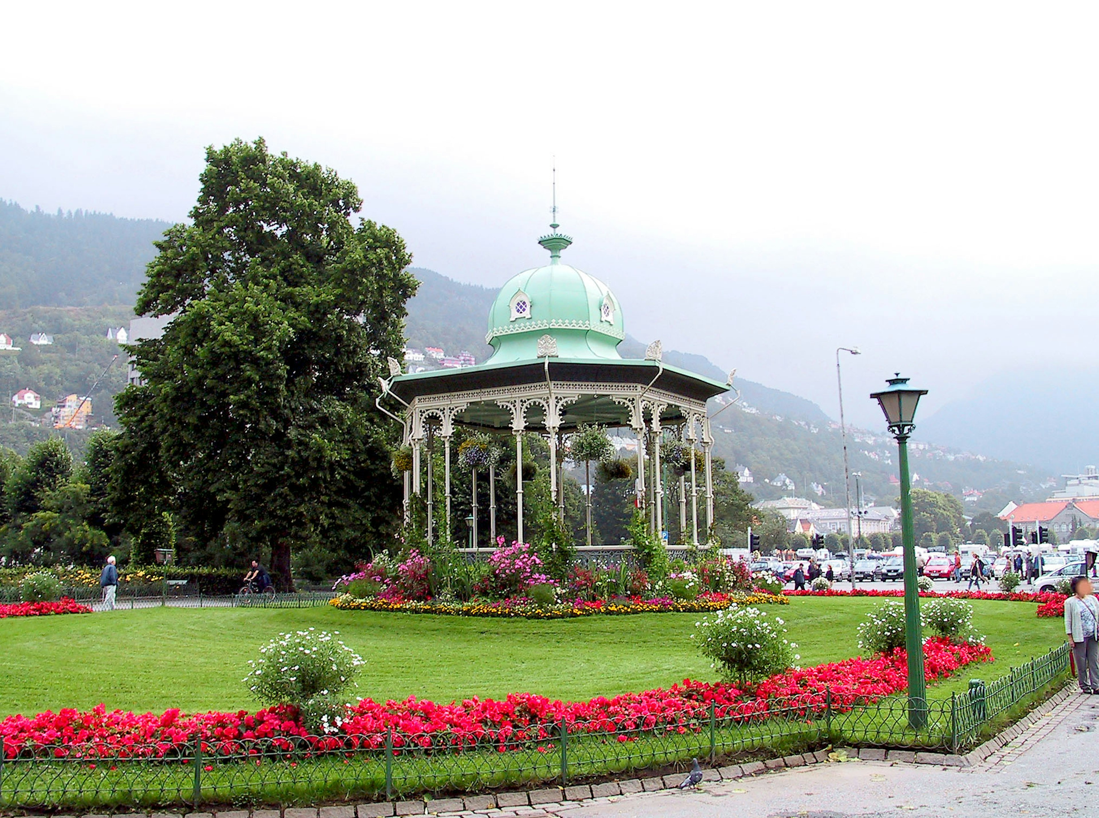 Green gazebo in a park surrounded by colorful flowers