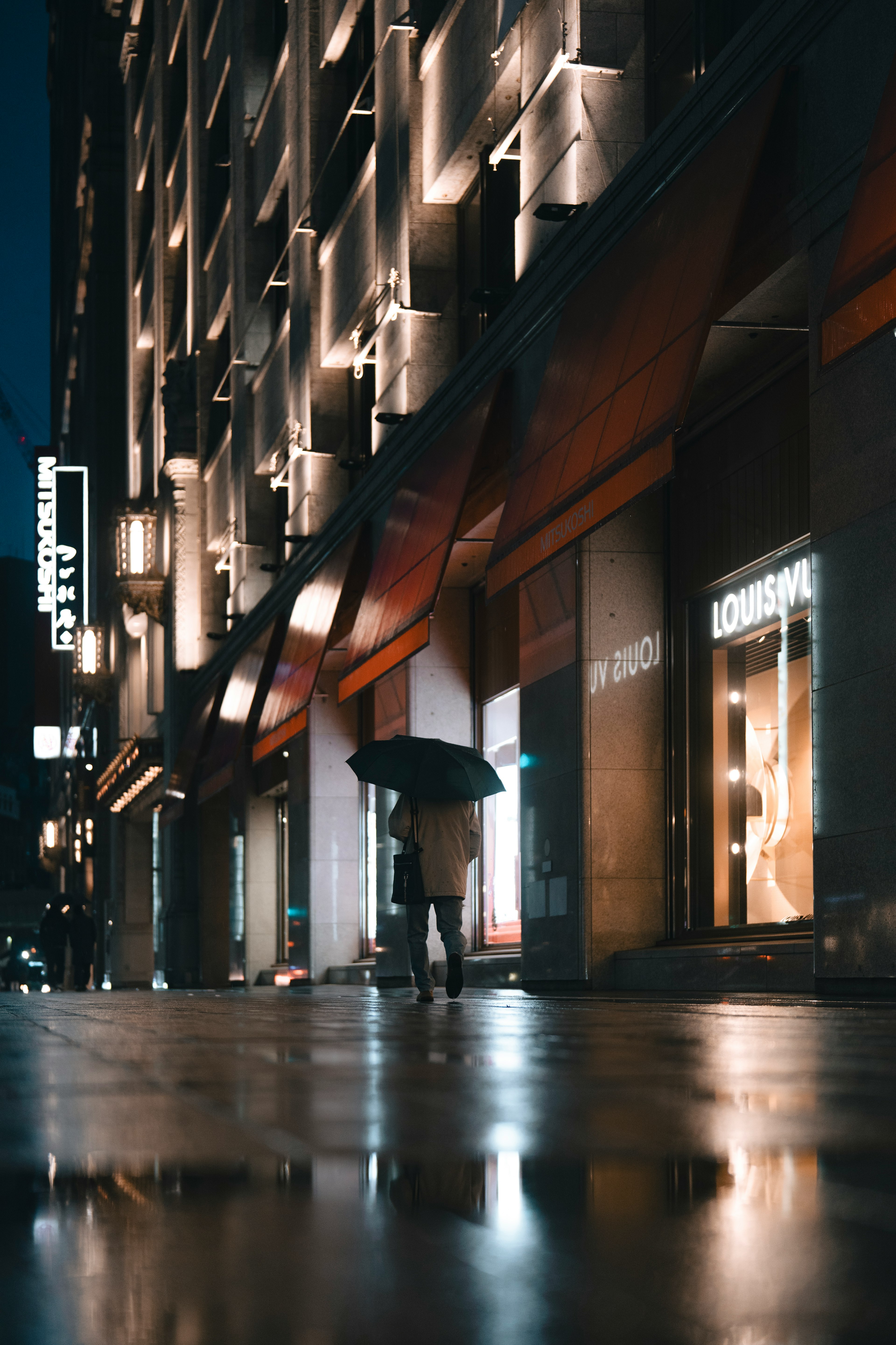 Eine Person mit einem Regenschirm in einer nächtlichen Stadtumgebung mit hellen Ladenlichtern