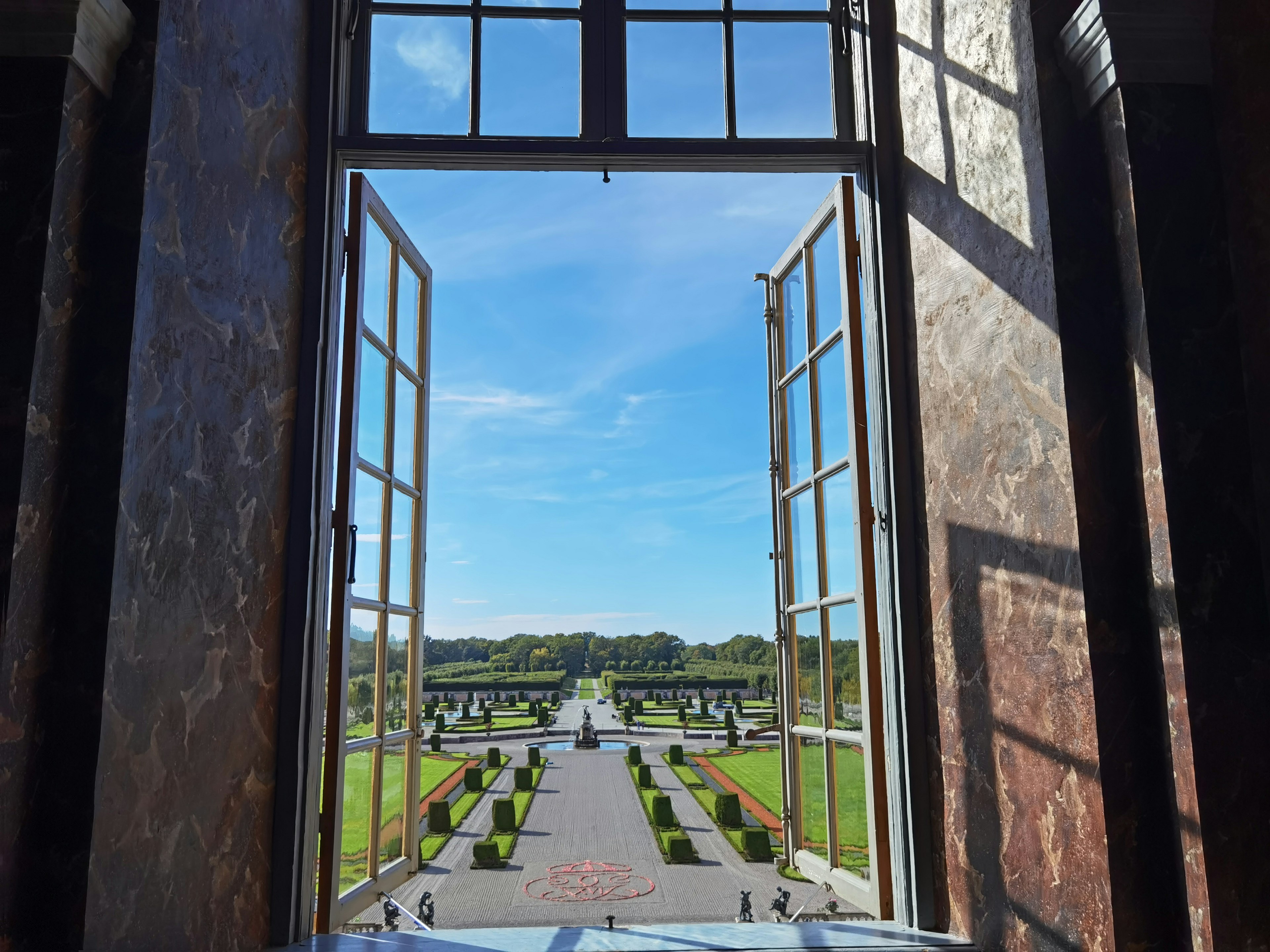 View from an open window showcasing a beautiful garden with blue sky and greenery