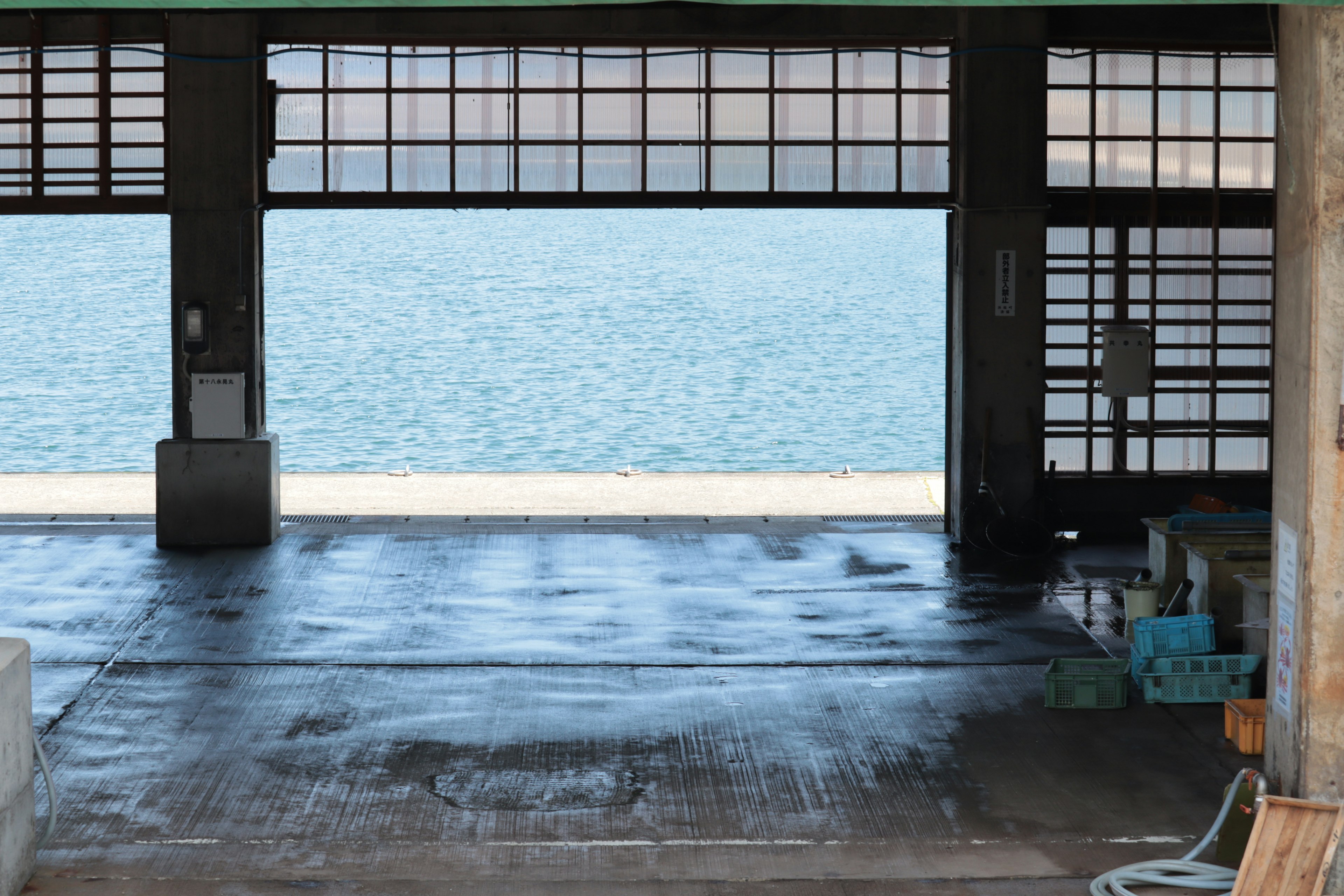 Interior of an open warehouse with a view of water grid-patterned windows and wet floor