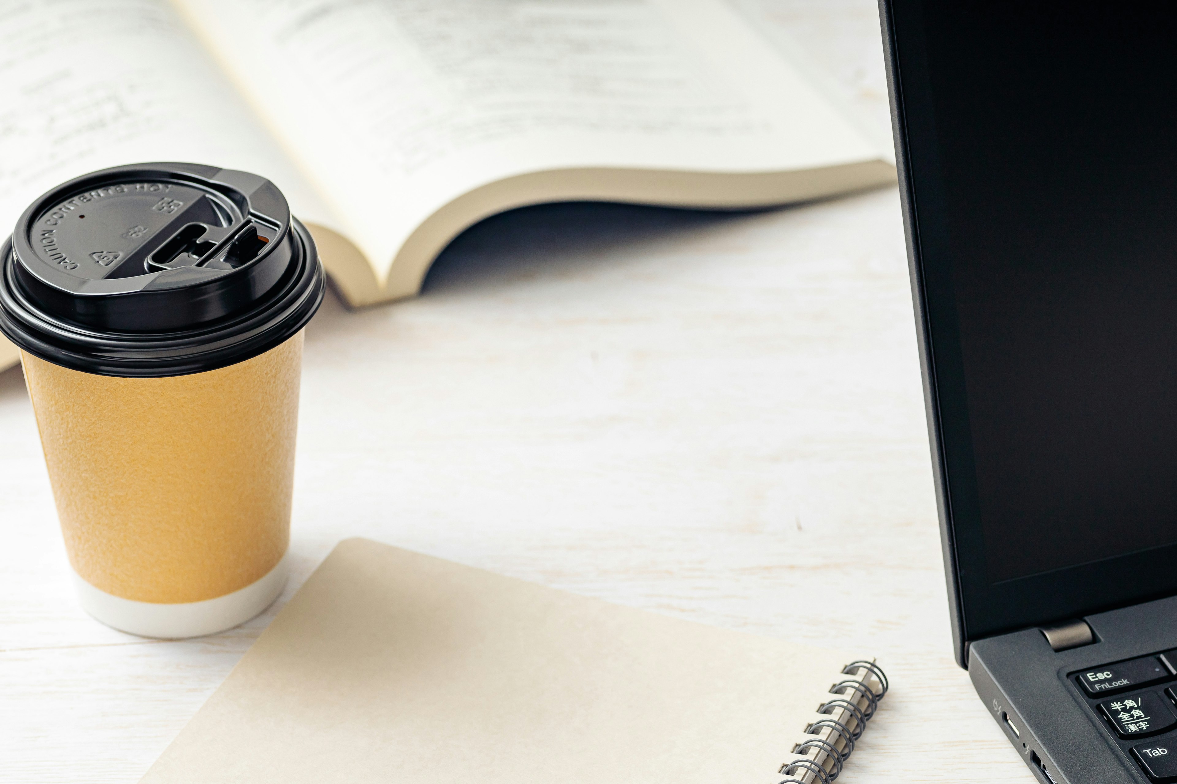 Workspace featuring a coffee cup, an open book, and a laptop