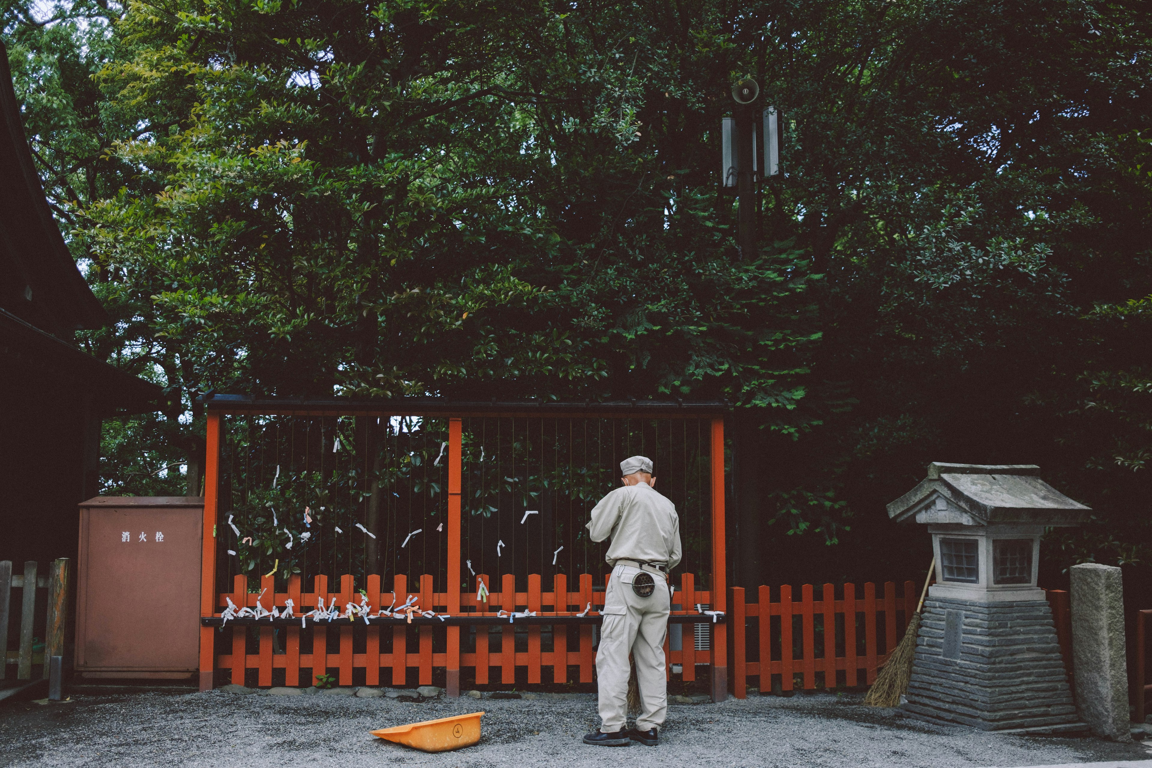 一个男人在神社祈祷，周围是绿色的树木和独特的红色围栏