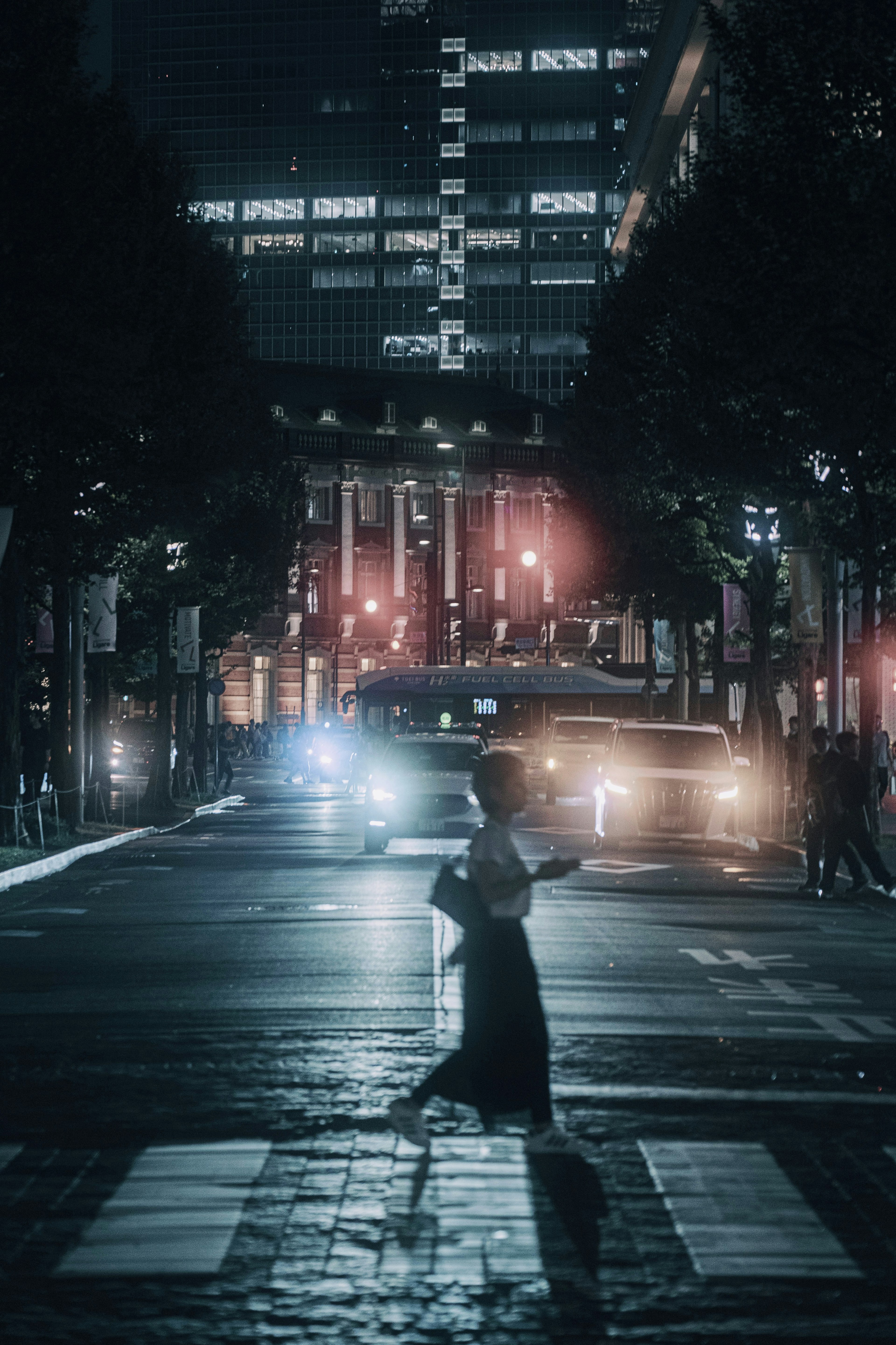 A person crossing the street in a city at night with illuminated vehicles