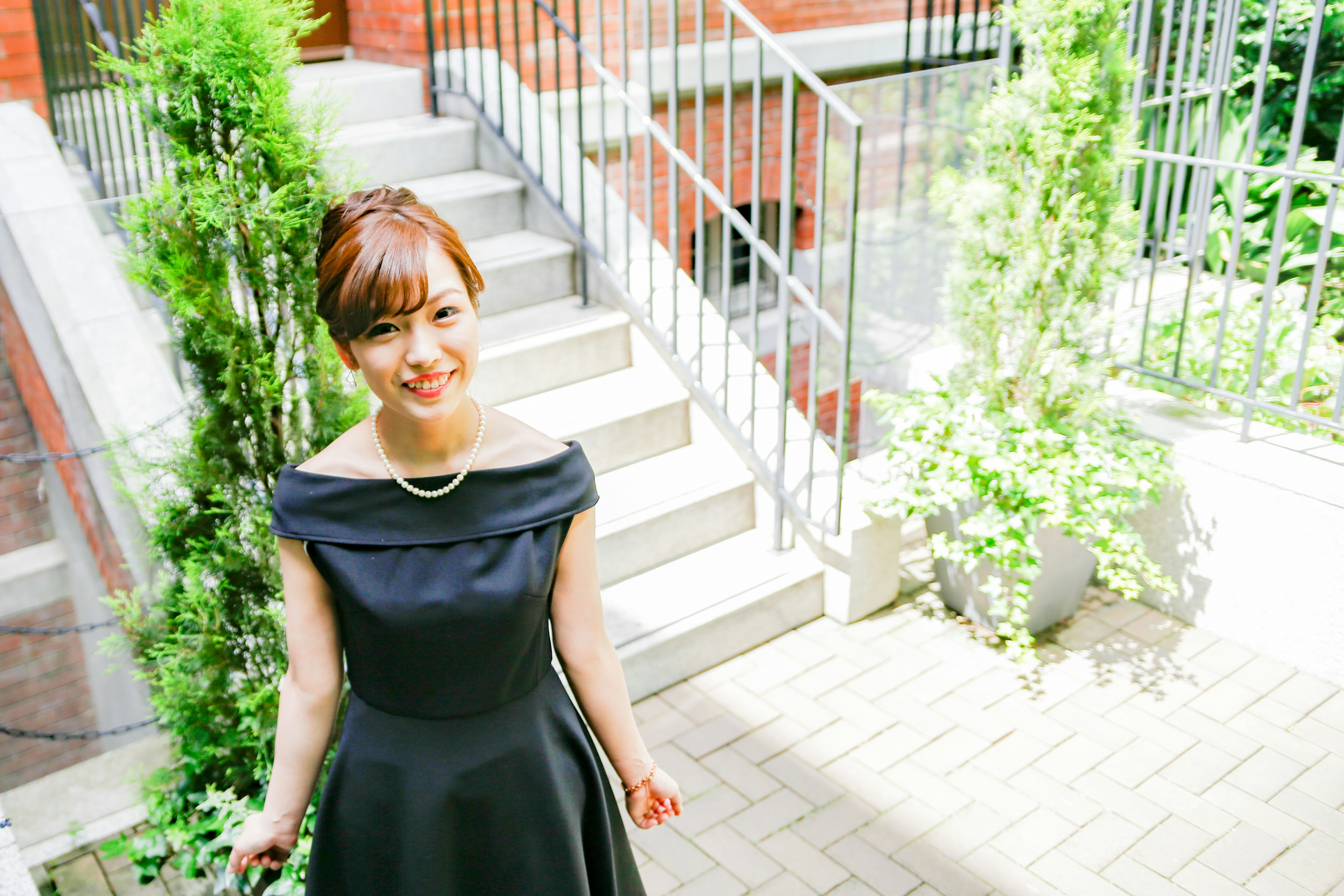 A woman in a black dress smiling in front of stairs with greenery