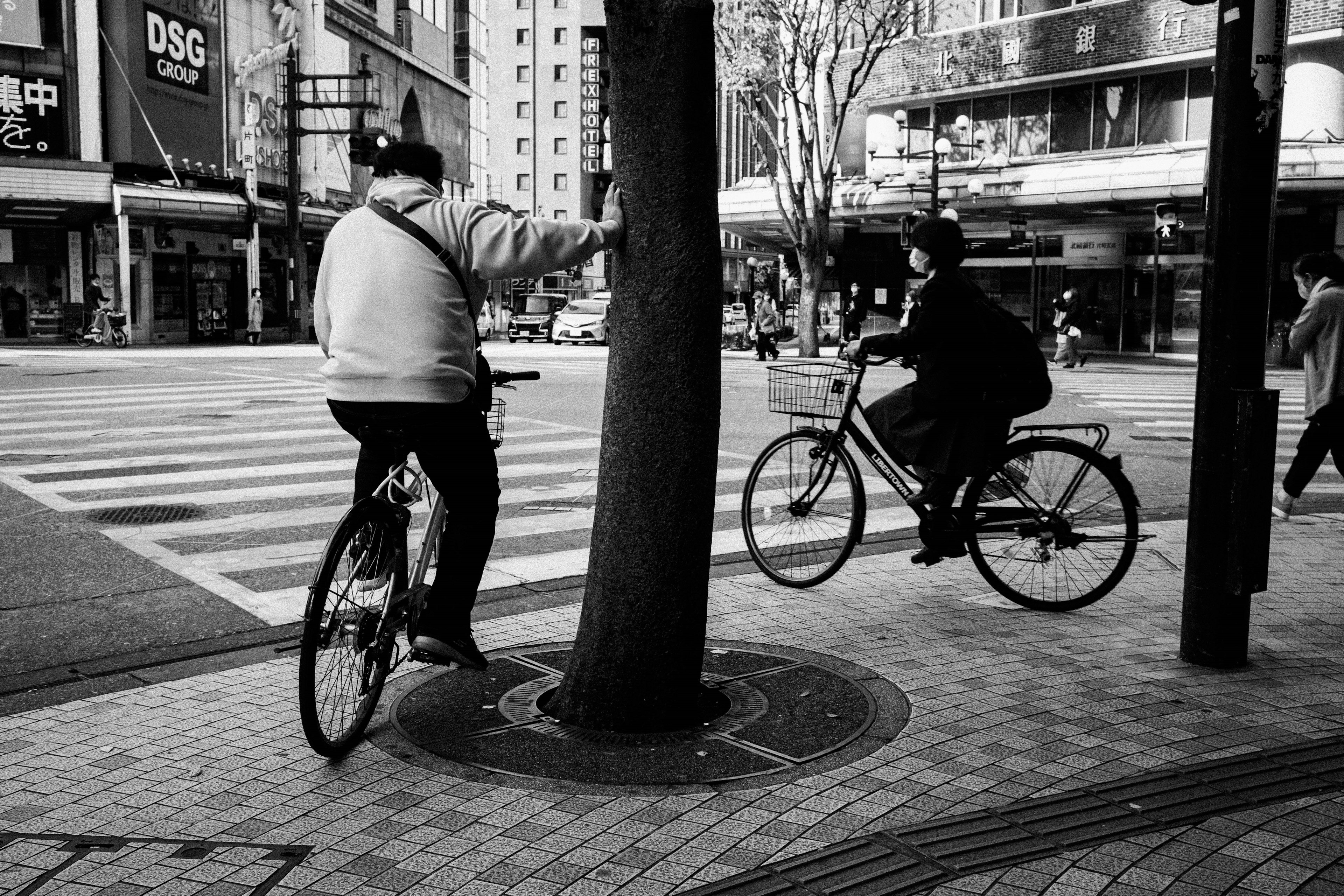 Two individuals on bicycles facing each other at a crosswalk in a black and white urban setting