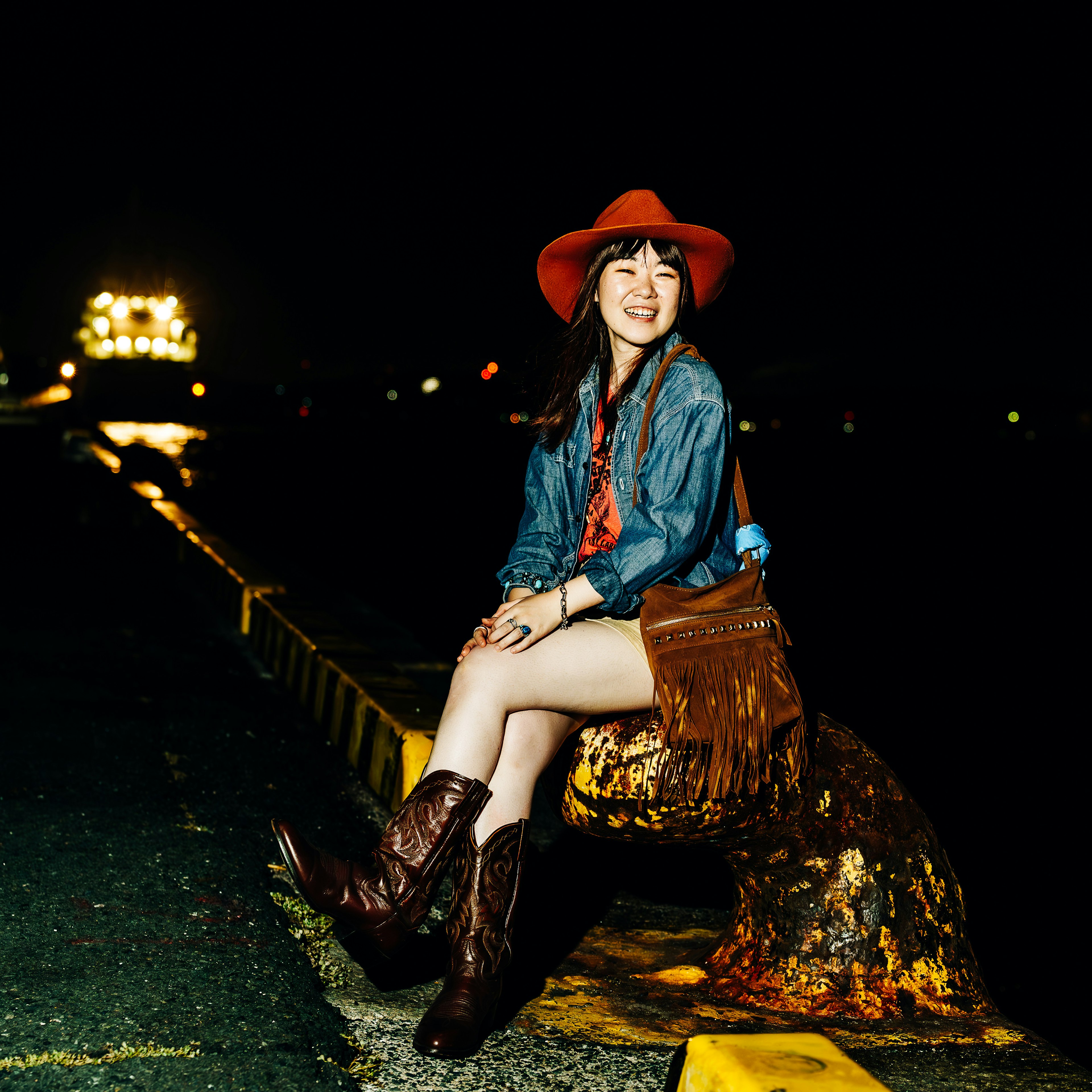 A woman wearing a red hat and cowboy boots sitting at a night port