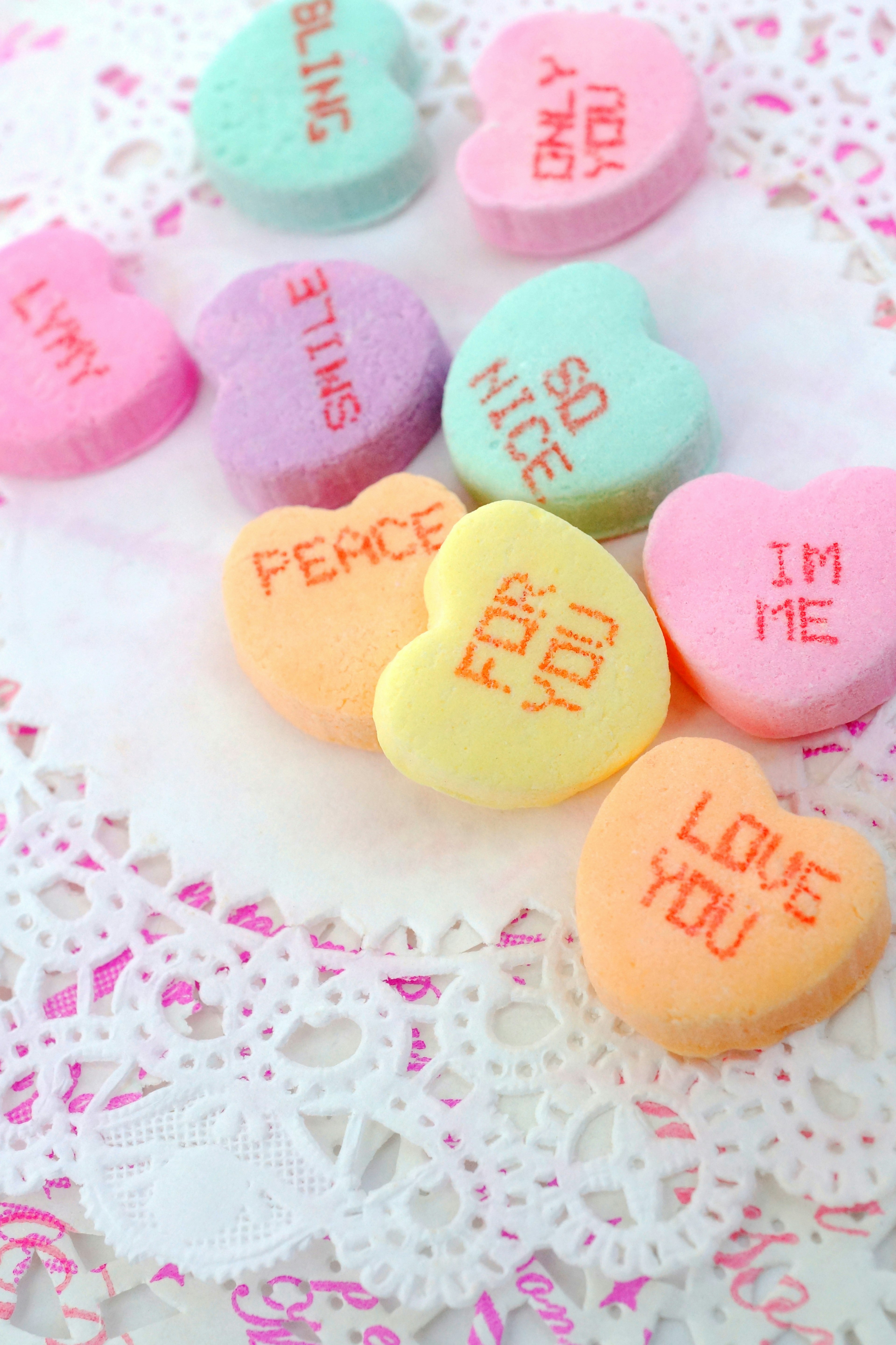 Bonbons en forme de cœur colorés disposés sur de la dentelle avec des messages d'amour et d'amitié imprimés sur chaque bonbon