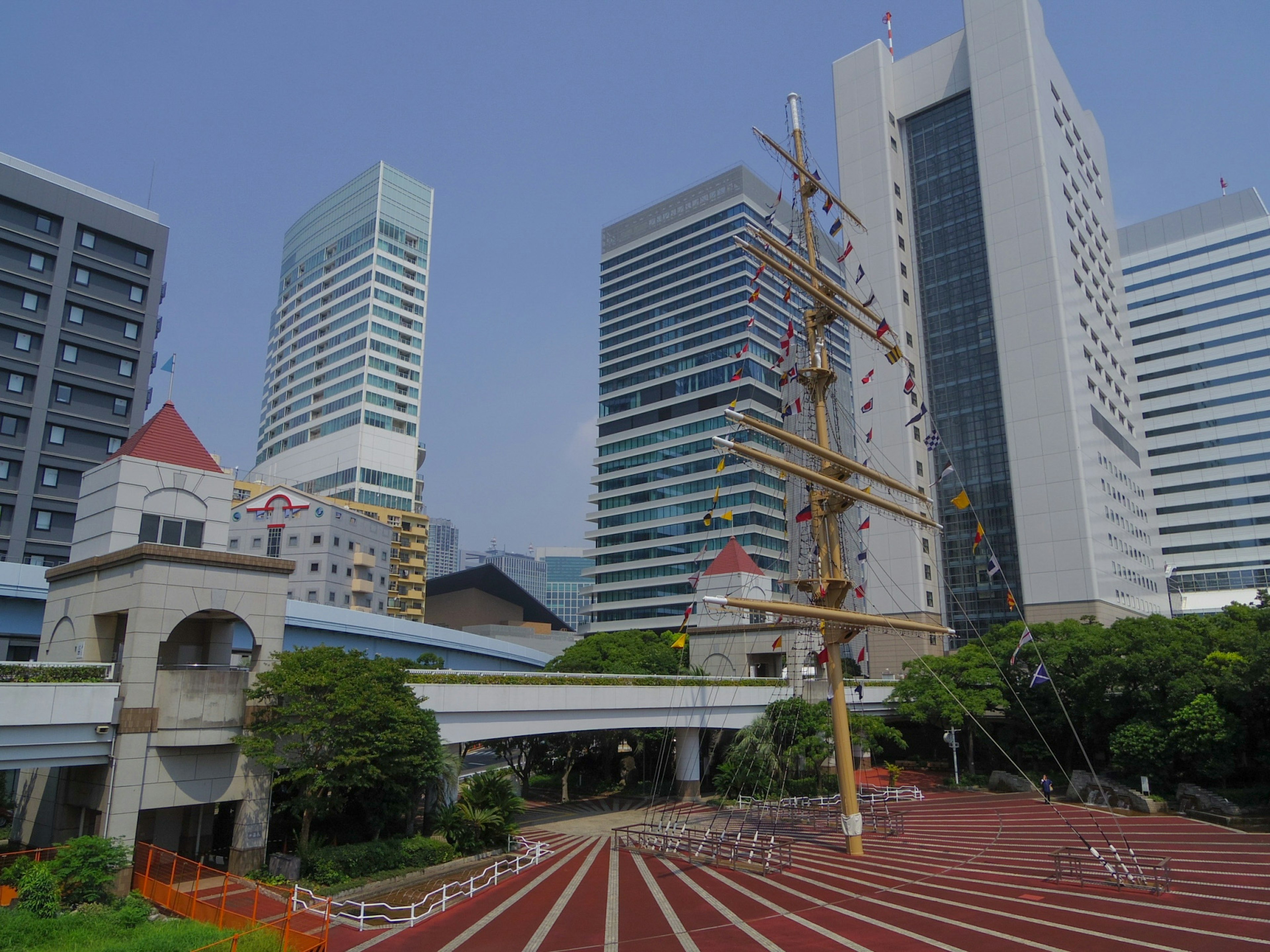 Urban landscape featuring modern buildings and a park with a tall ship mast