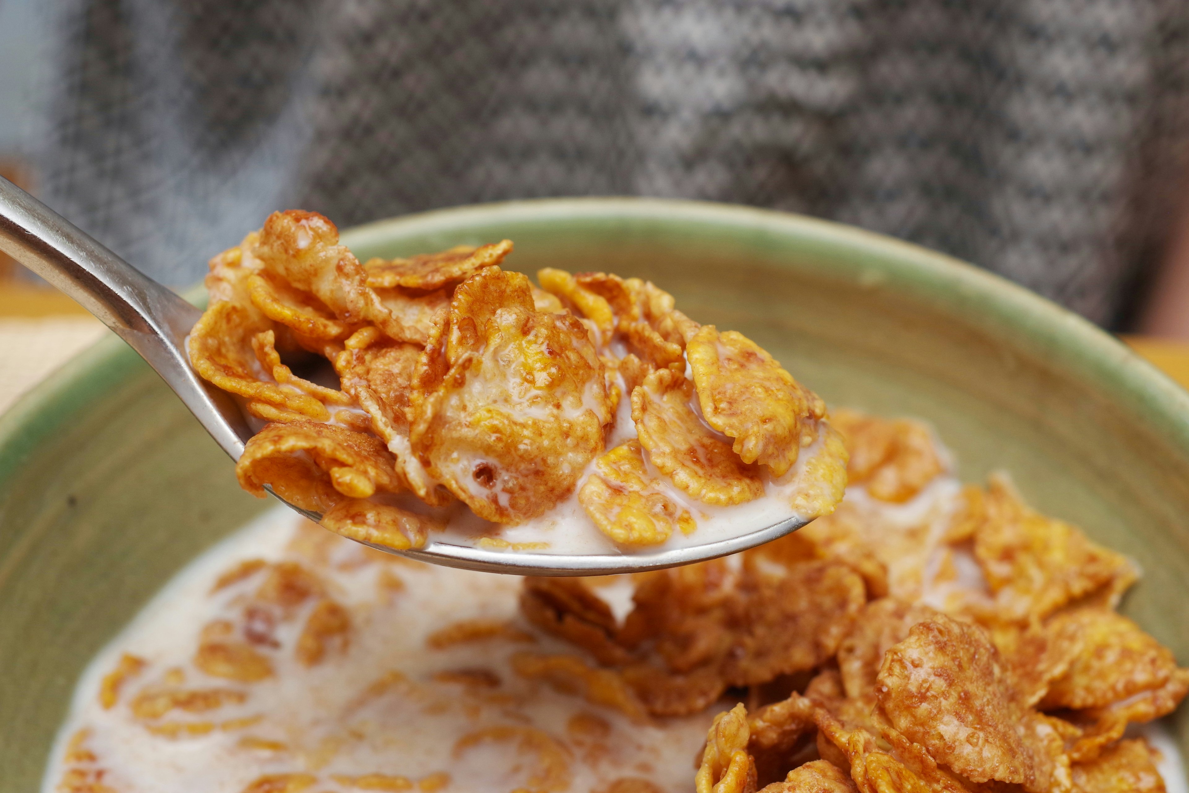 A spoonful of cornflakes with milk in a green bowl