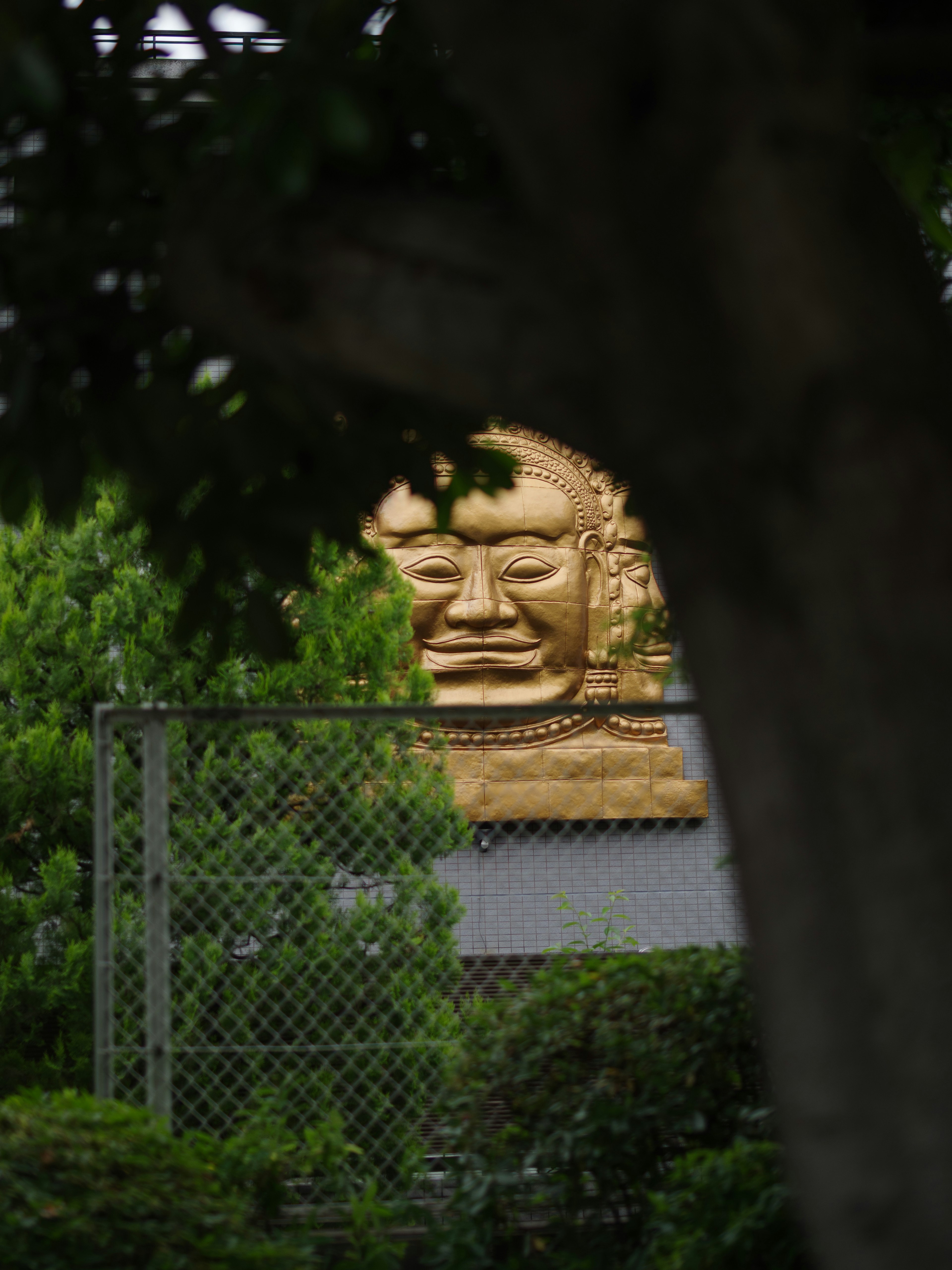 Sculpture de visage doré visible à travers les arbres