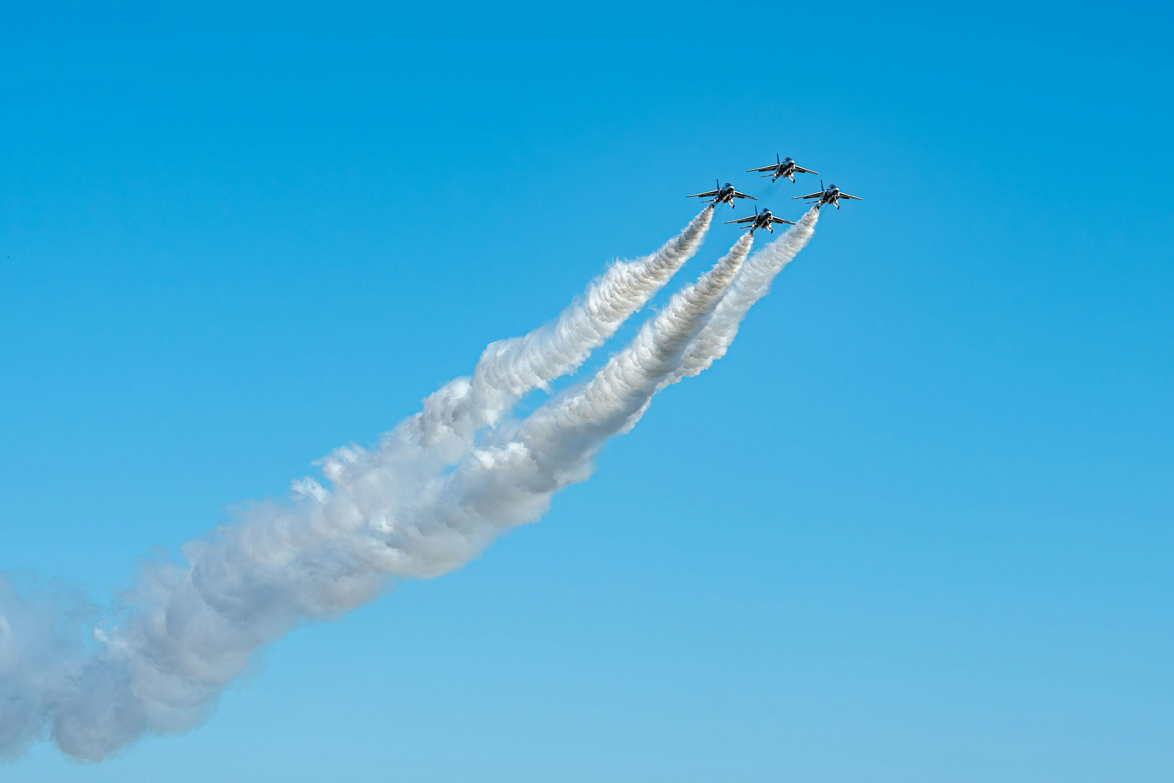 Cinco aviones de combate ascendiendo con estelas de humo contra un cielo azul