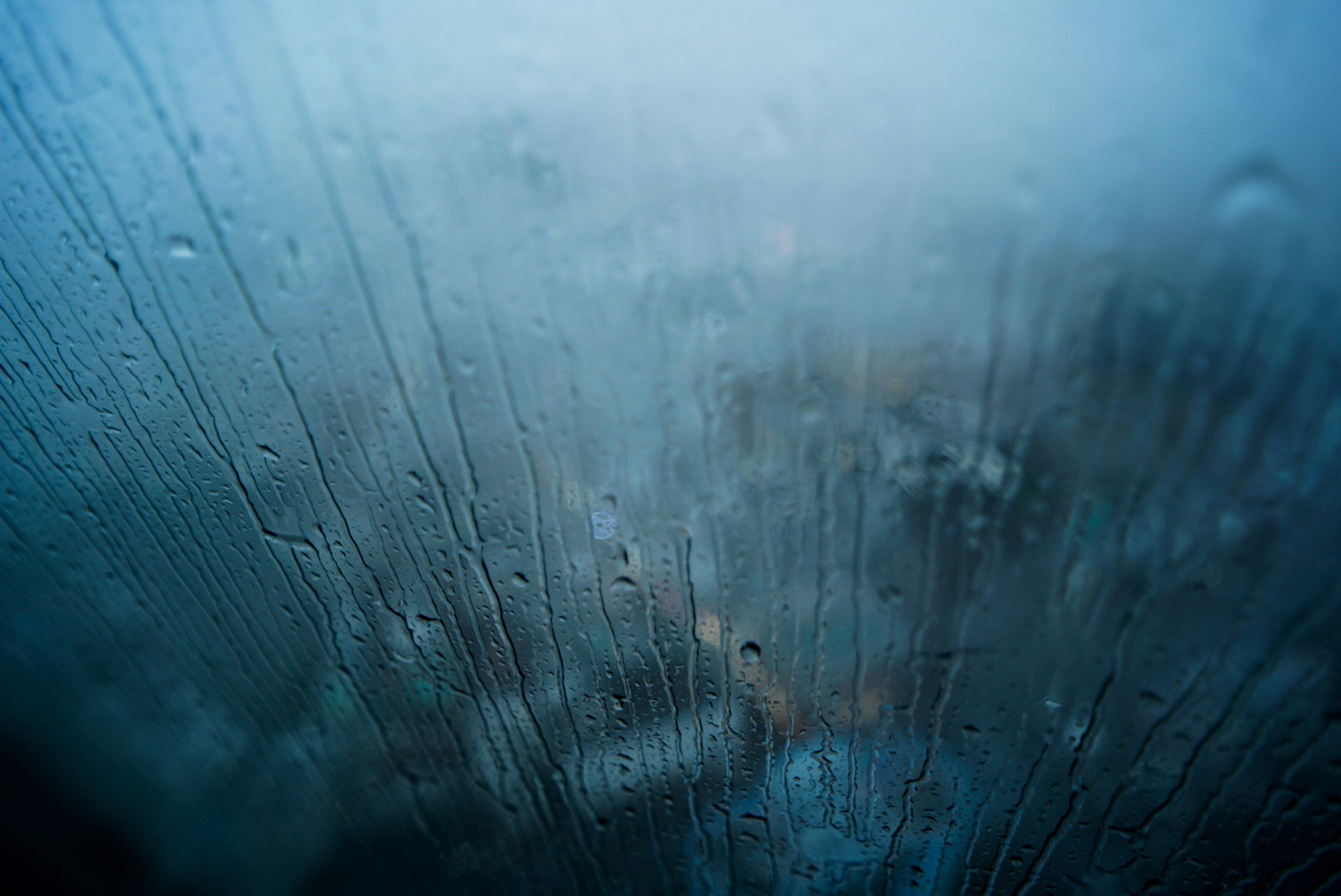 Immagine di gocce d'acqua su una finestra appannata con uno sfondo blu