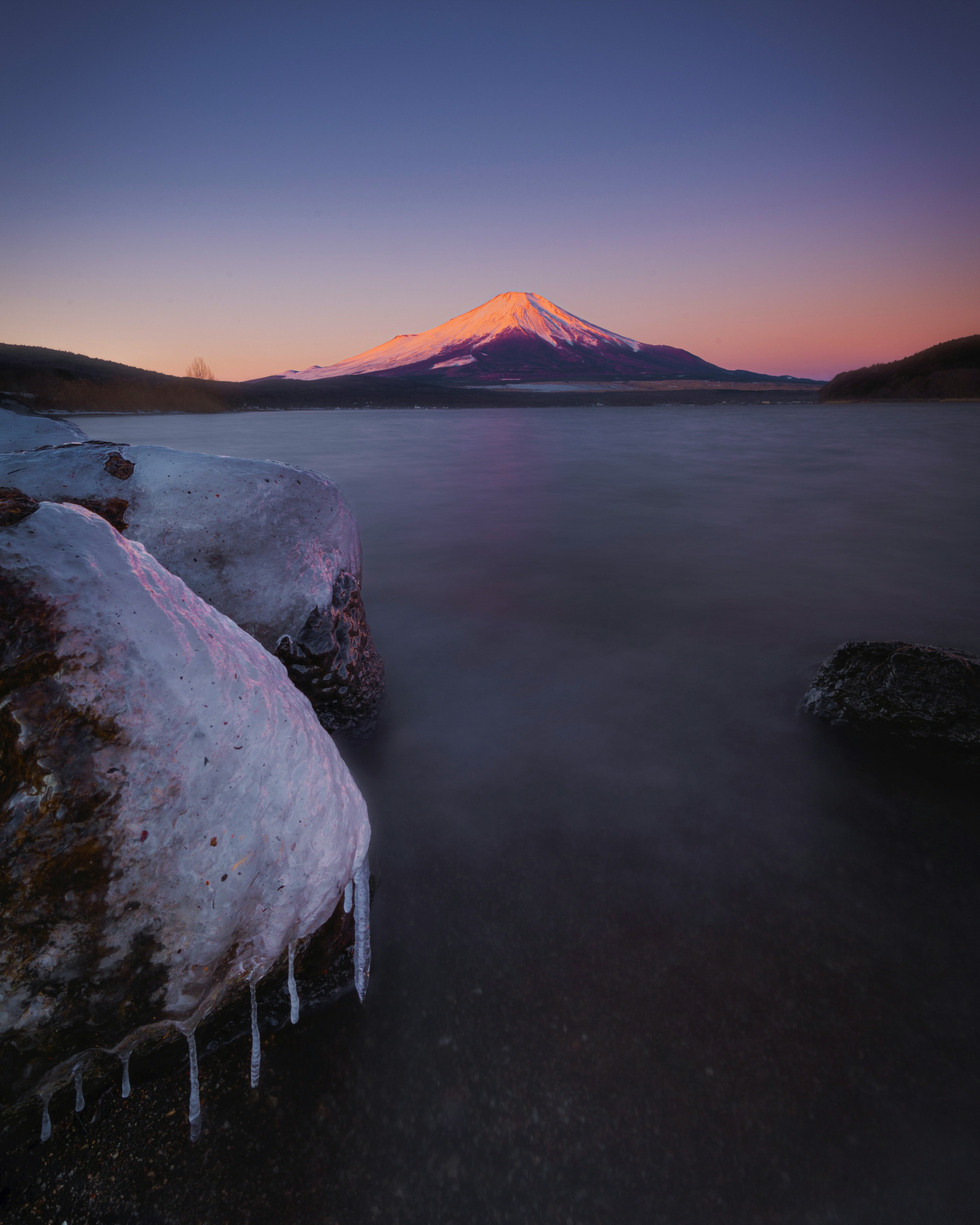 Roccia coperta di neve e lago ghiacciato in primo piano con un bellissimo paesaggio montano