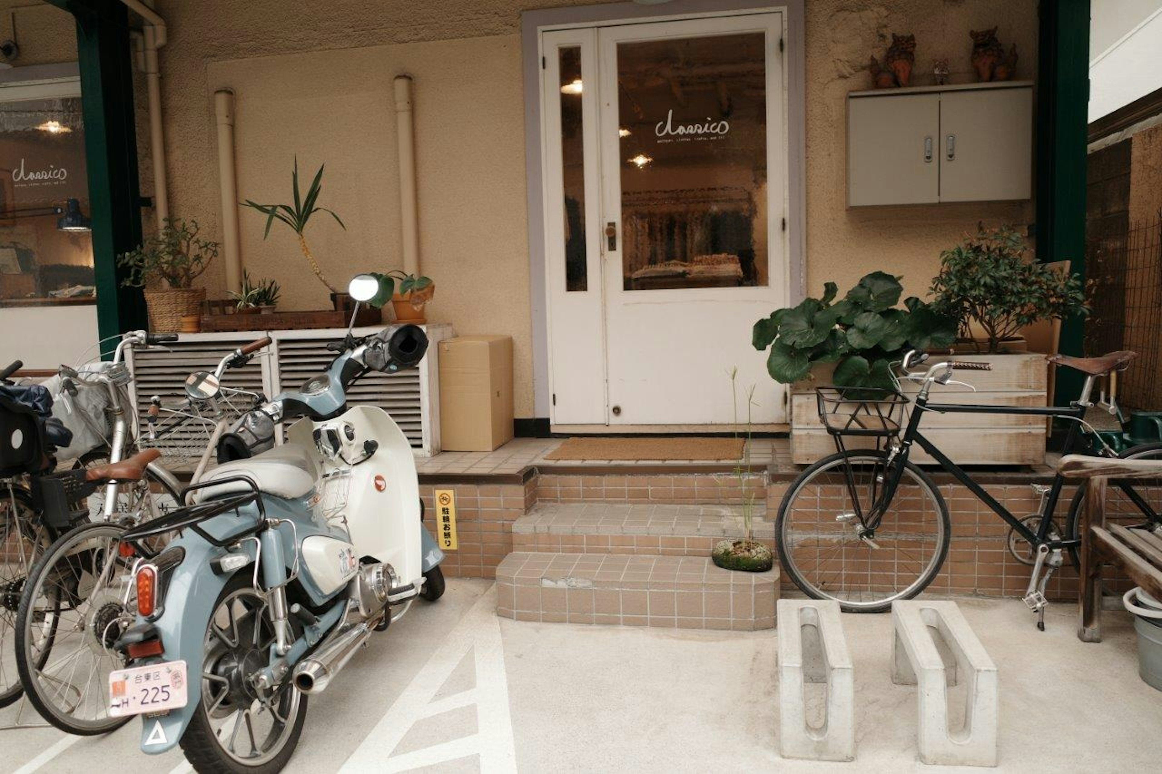 Entrada de café con bicicletas y scooter plantas en macetas decorativas