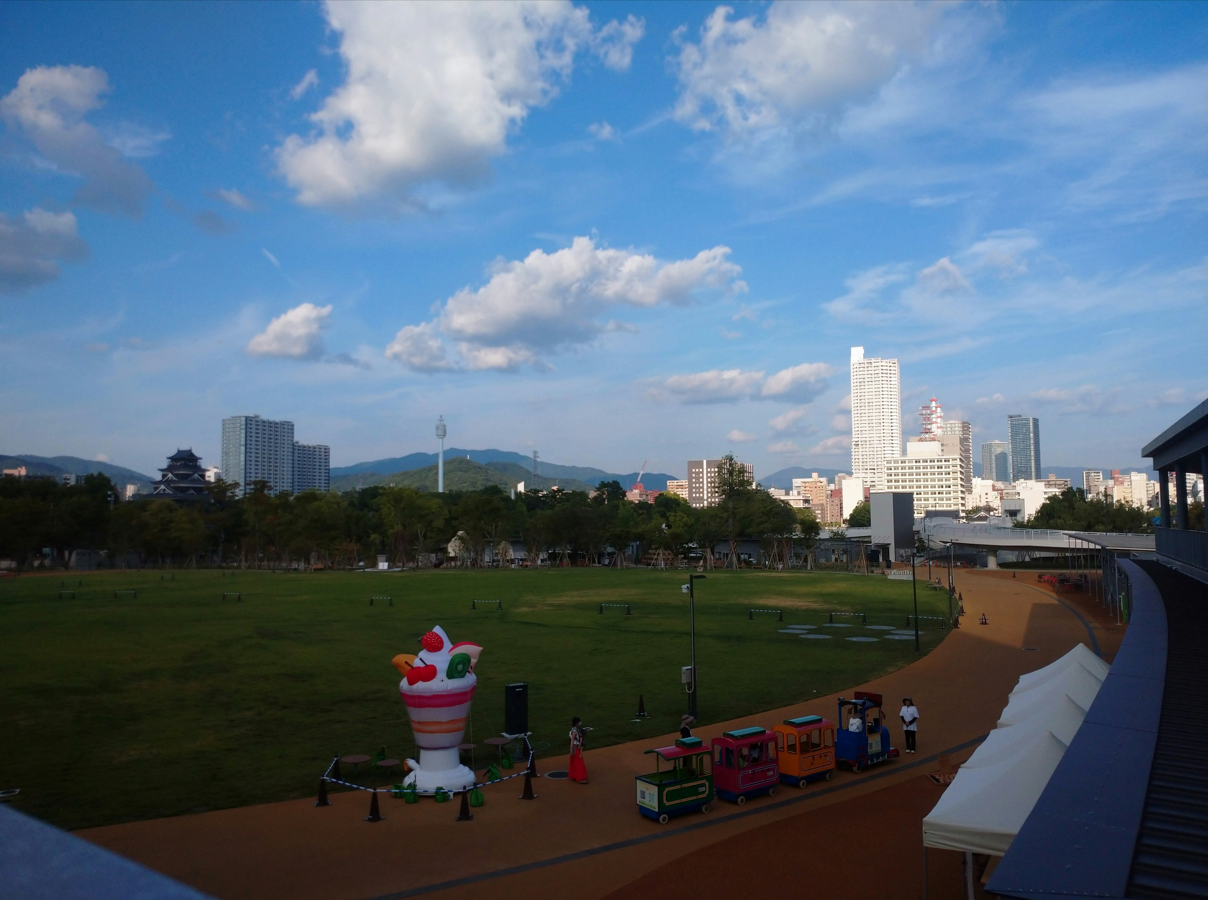 Vue pittoresque d'un parc avec ciel bleu et nuages présentant des équipements de jeux colorés et de grands bâtiments