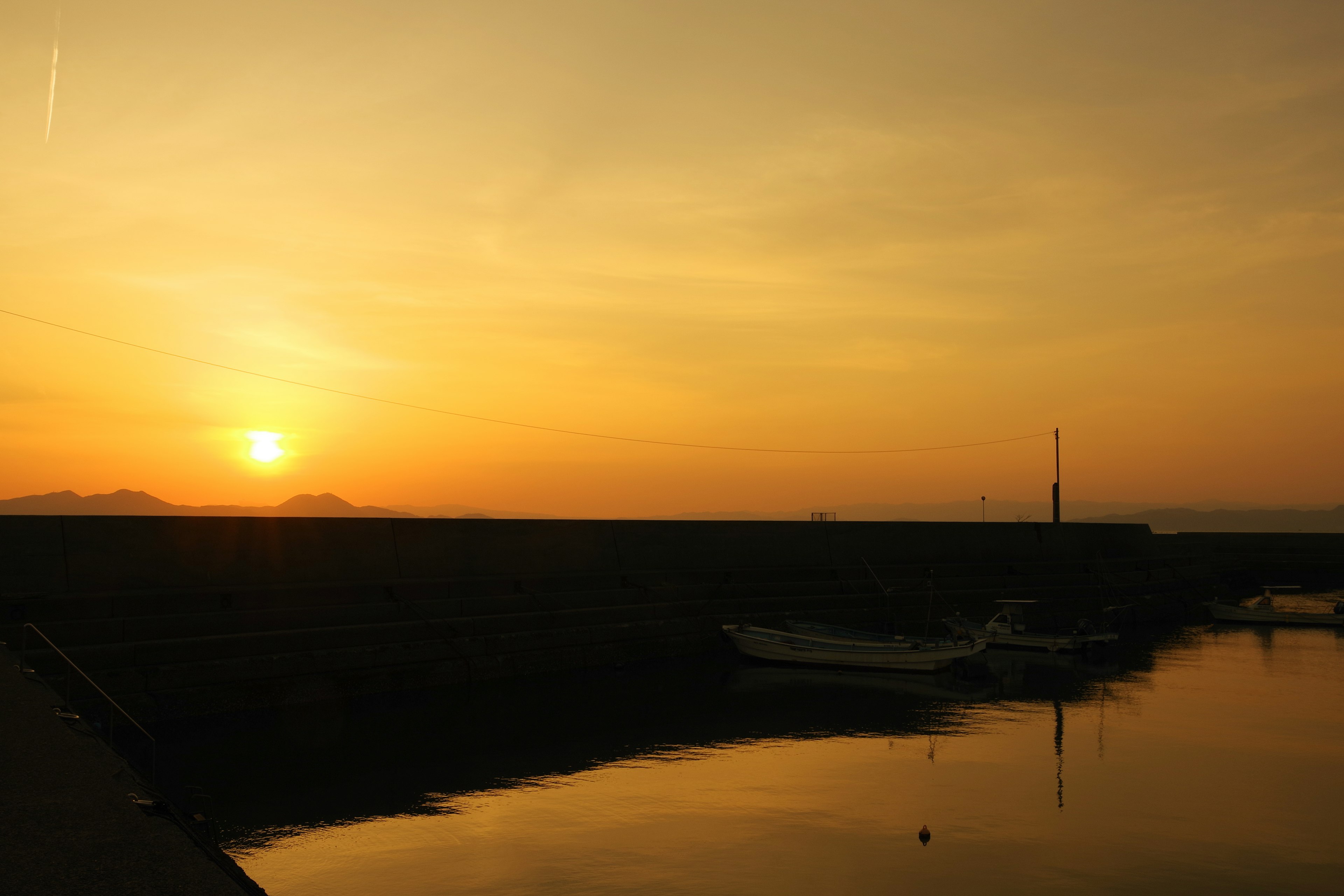 Escena de atardecer costero con barcos amarrados en una superficie de agua tranquila