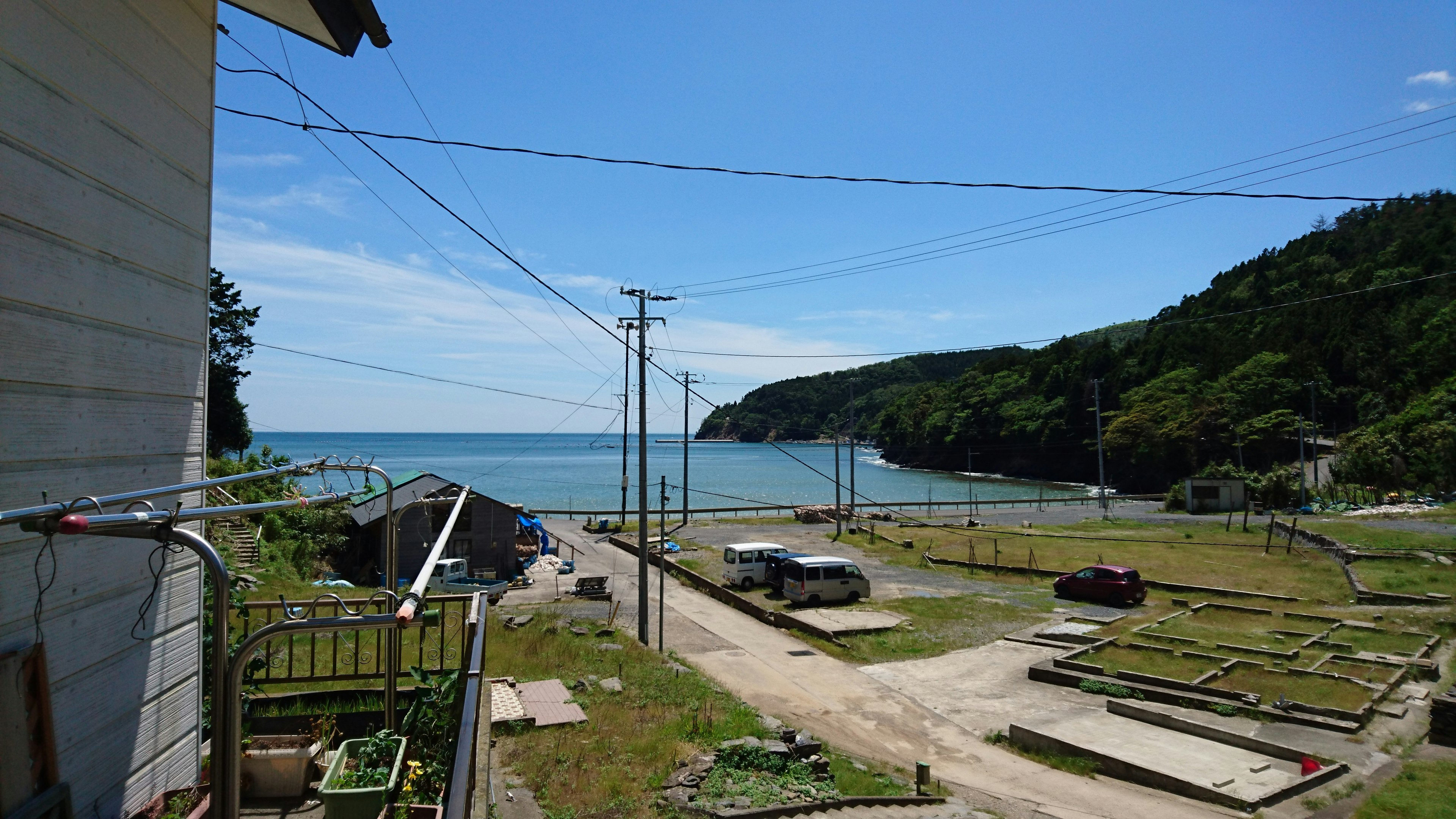 Landschaftliche Aussicht auf das Land mit blauem Meer und grünen Hügeln geparkten Autos und Stromleitungen