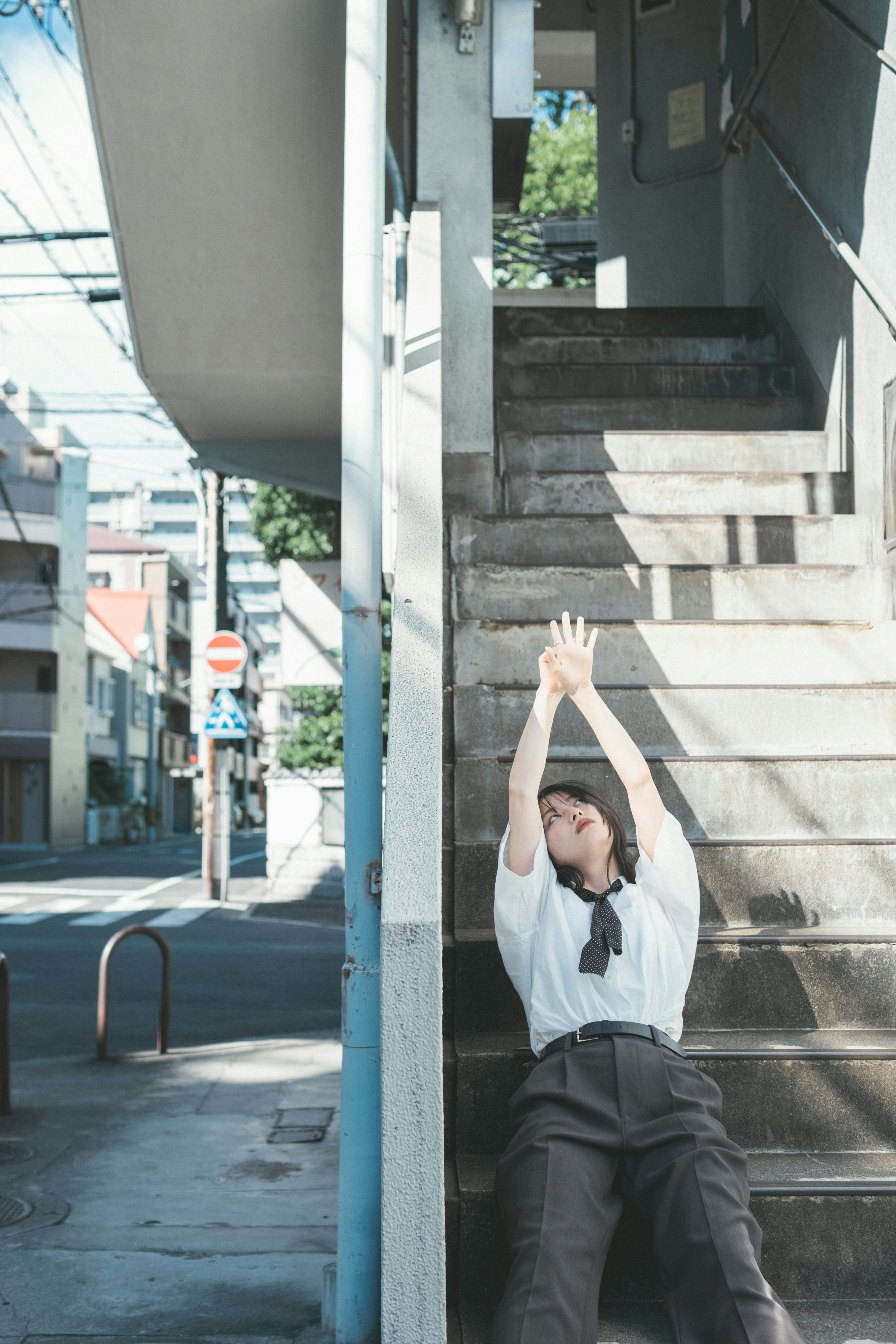 階段の側に座る女性の姿彼女は手を上に伸ばしている周囲には街の風景が広がっている