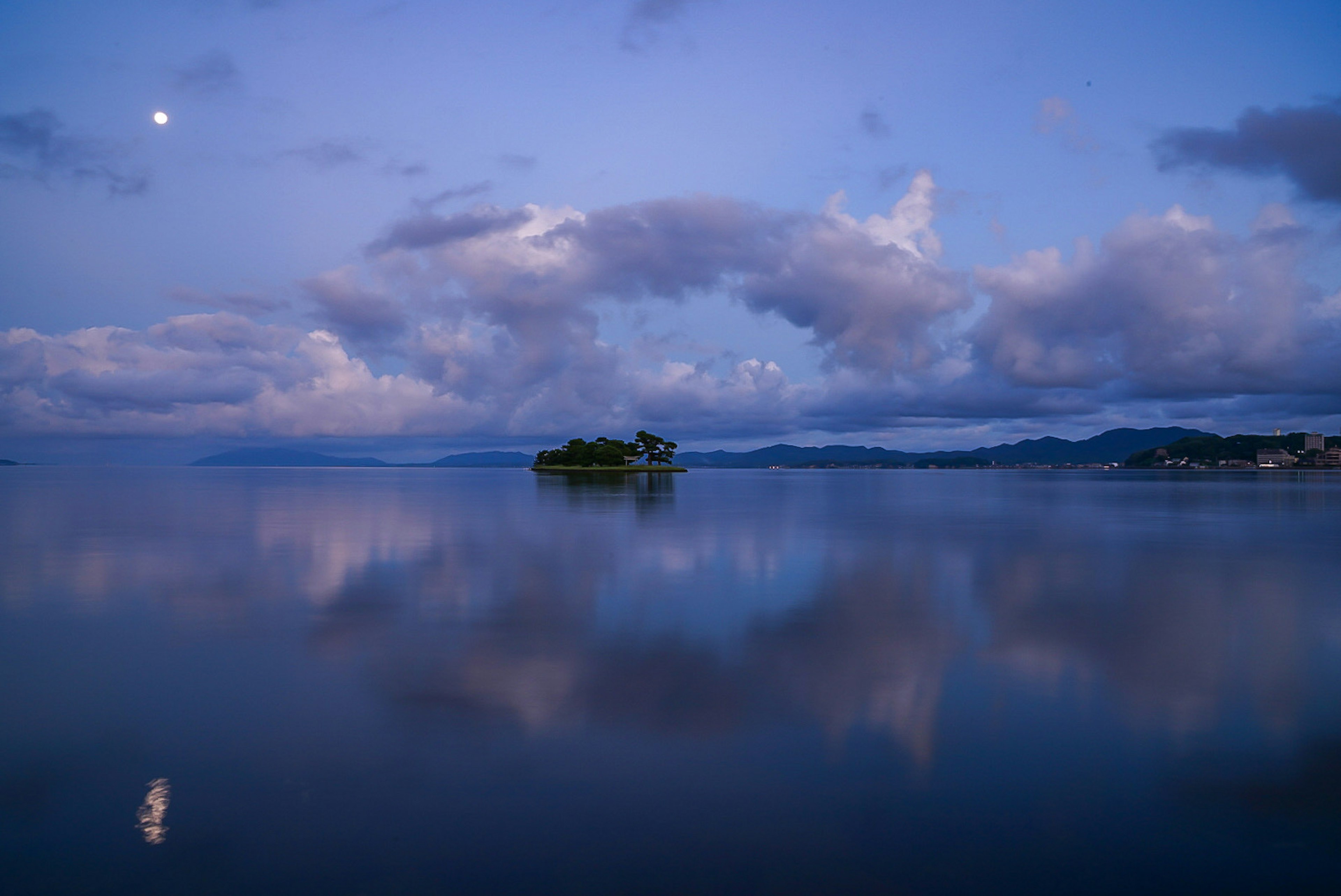 Calm lake reflecting blue sky and clouds Moon shining in the scenery