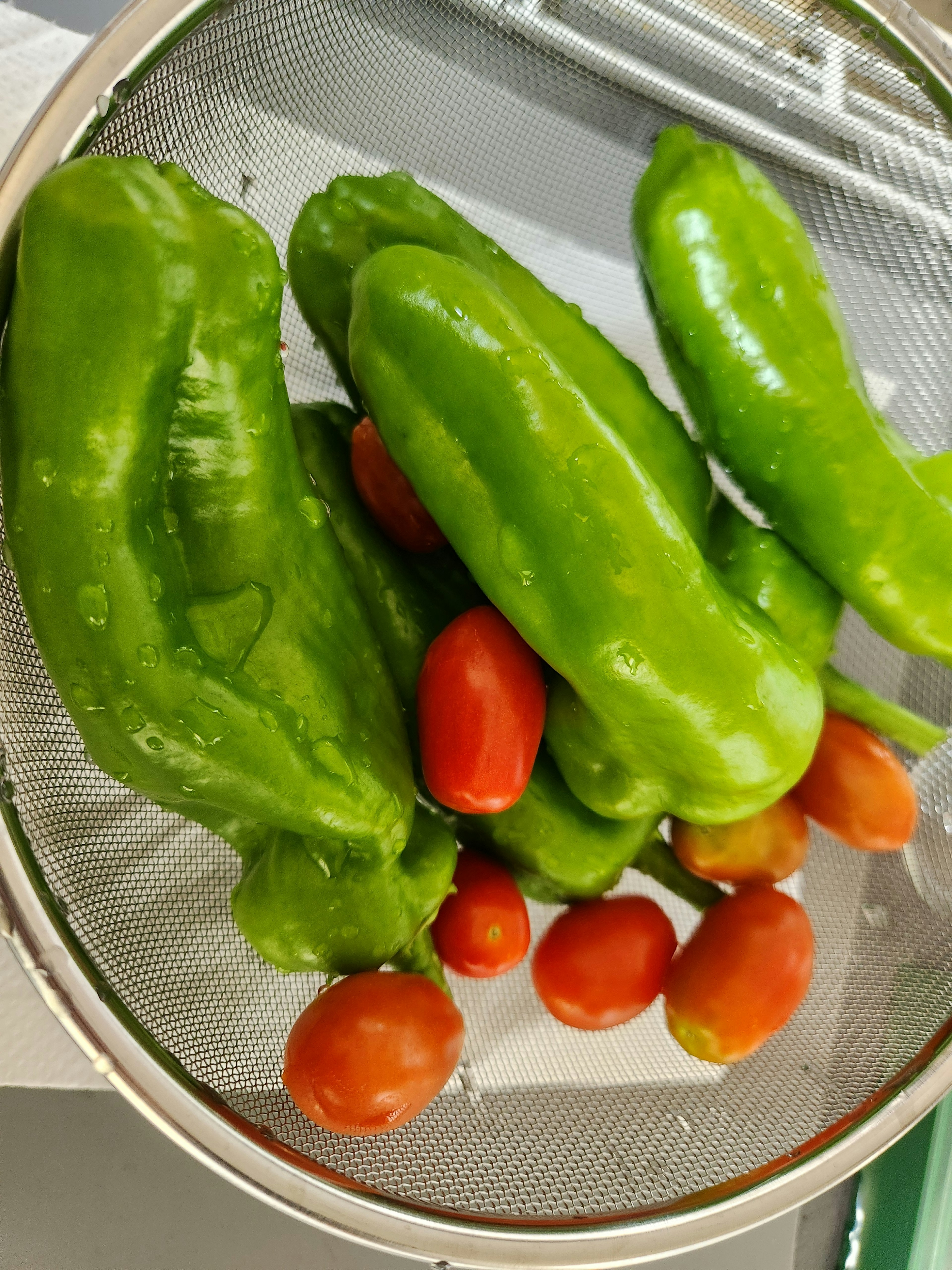 Green bell peppers and red cherry tomatoes in a colander