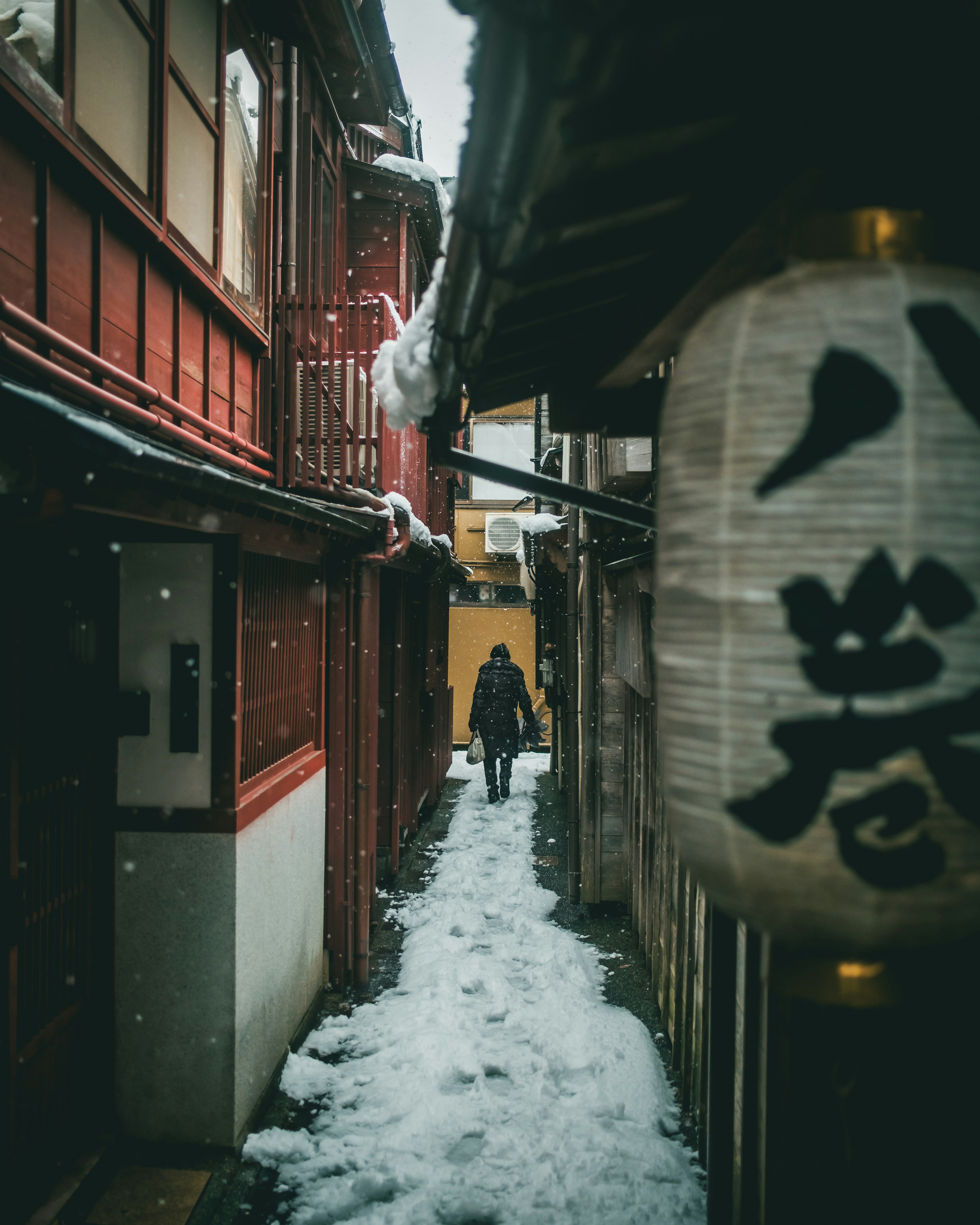 A person walking down a snowy alley with a lantern