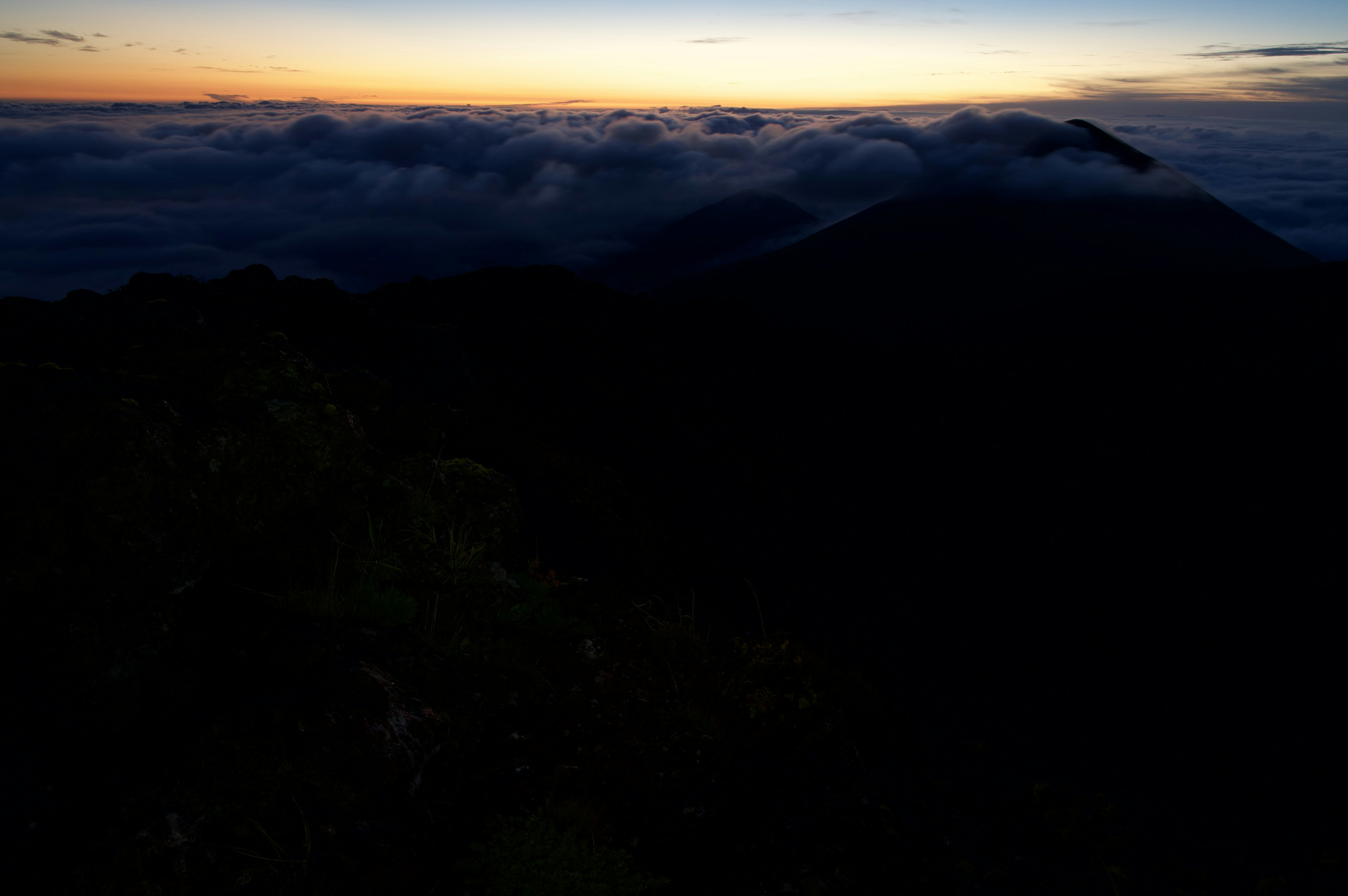 Dark mountain silhouette against a sea of clouds at sunset