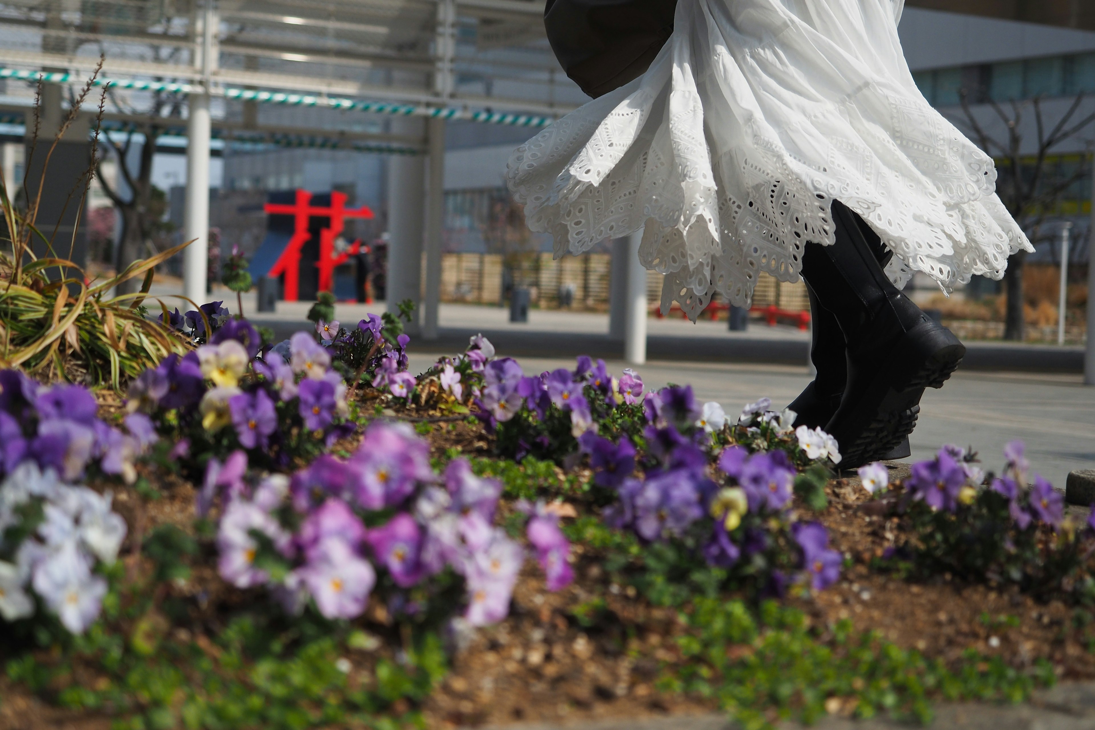 Une personne en robe blanche marchant devant des fleurs violettes